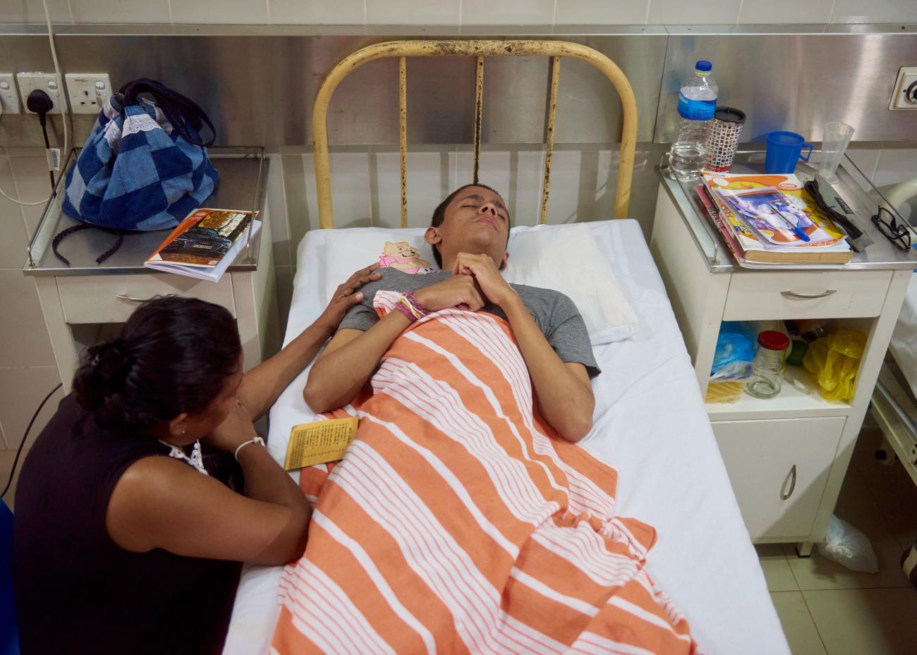 A mother prays next to her son in the learner’s ward, with his study books on both sides of the bed.