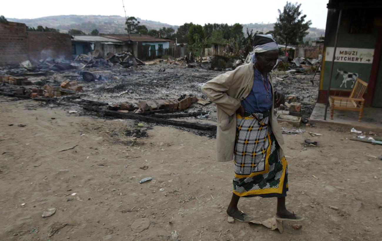 An elderly Kisii woman passes by the remains of a burned house.