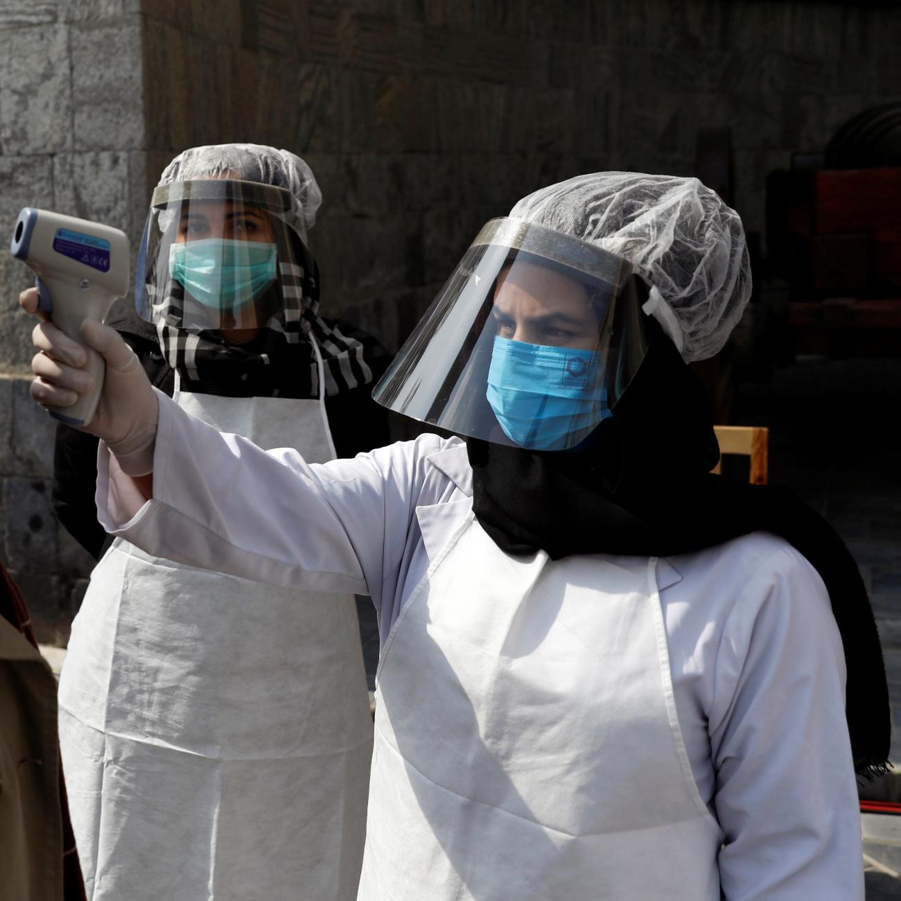 An Afghan health worker in protective gear checks the temperature of a woman before Afghanistan's President Ashraf Ghani inauguration as president, at the Presidential Palace in Kabul, Afghanistan March 9, 2020.