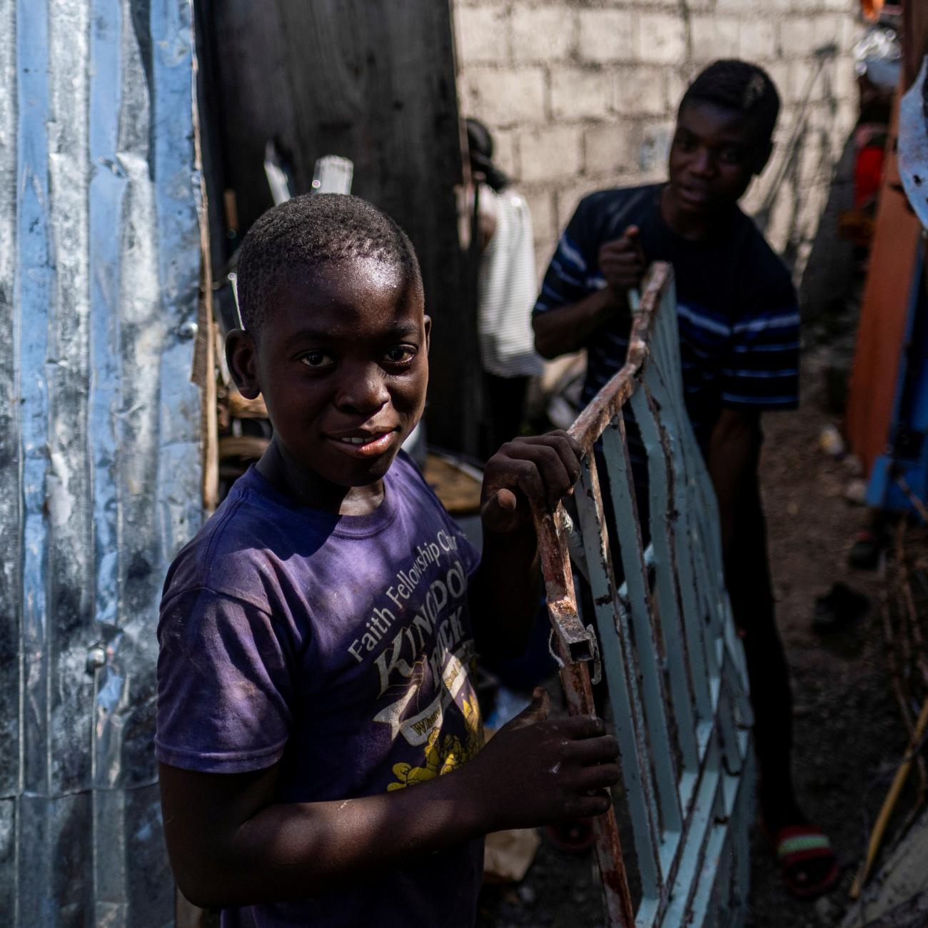 boys pick up scrap metal in the rubble of a destructed building