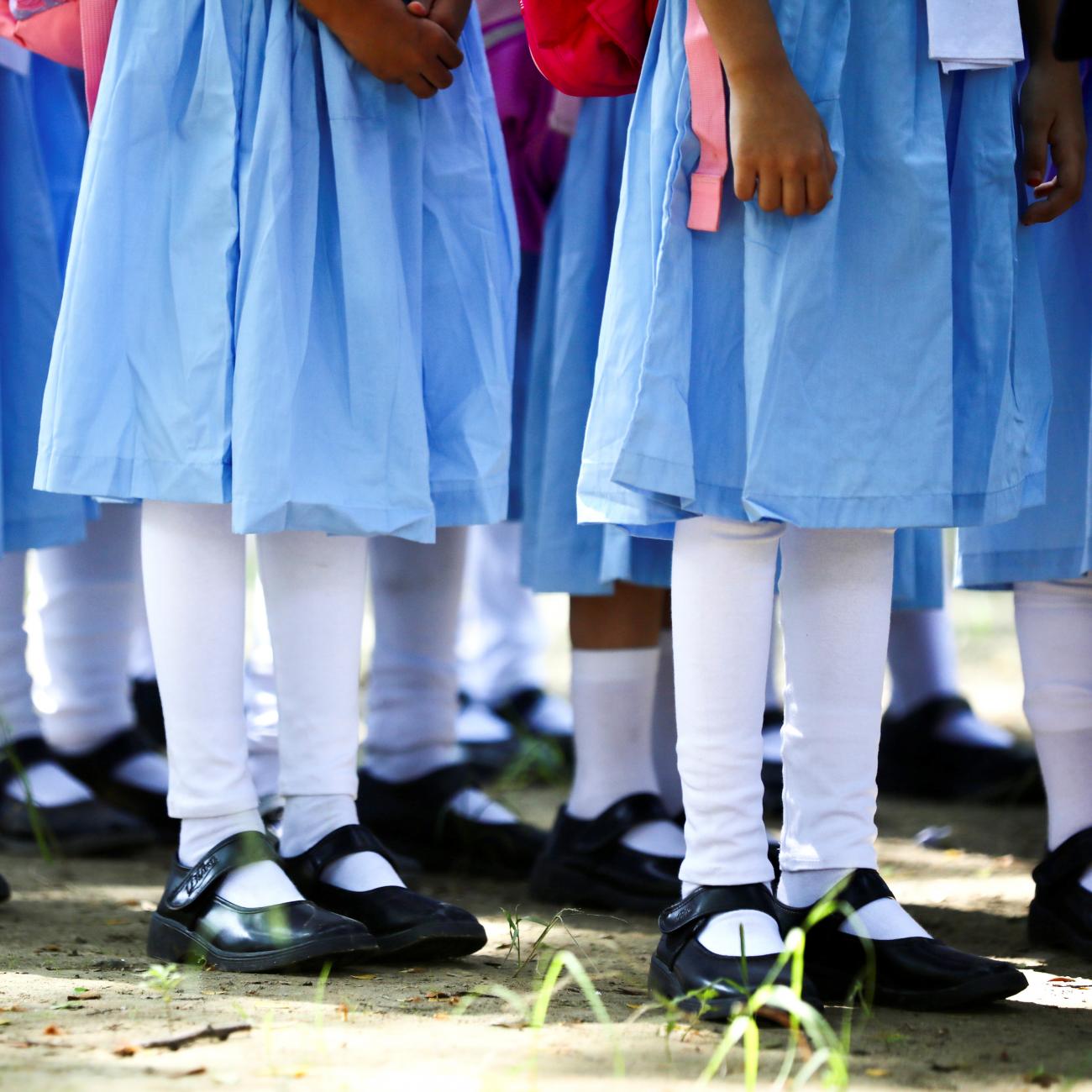 The legs and feet of students wearing blue dresses, white stockings, and black shoes can be seen standing in queues at the Viqarunnisa Noon School & College, in Dhaka, Bangladesh, September 12, 2021. 