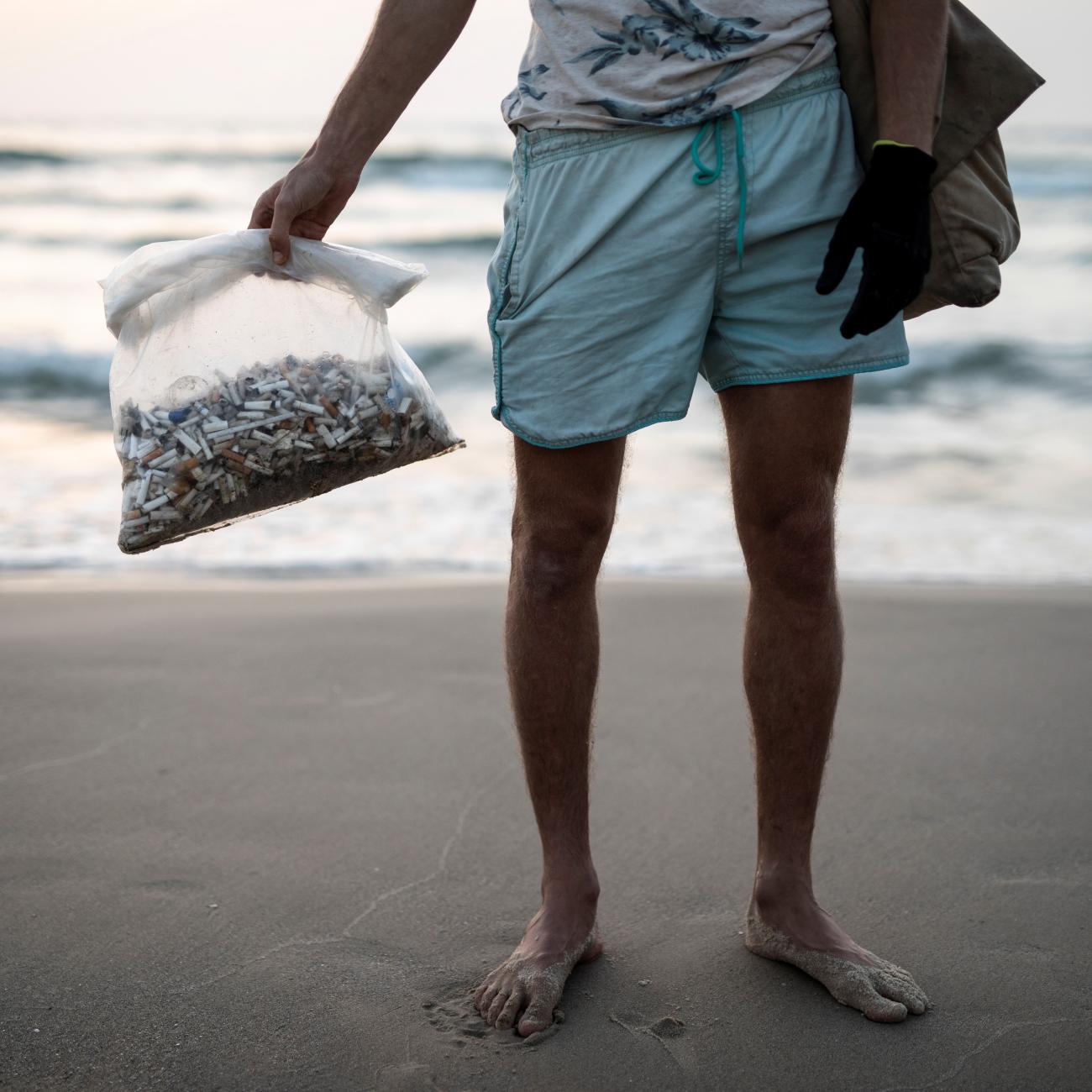 Julian Melcer (only his lower body can be seen) holds a plastic bag filled with cigarette butts he collected from the shore of the Mediterranean Sea at a beach in Tel Aviv, Israel, on April 20, 2021. 