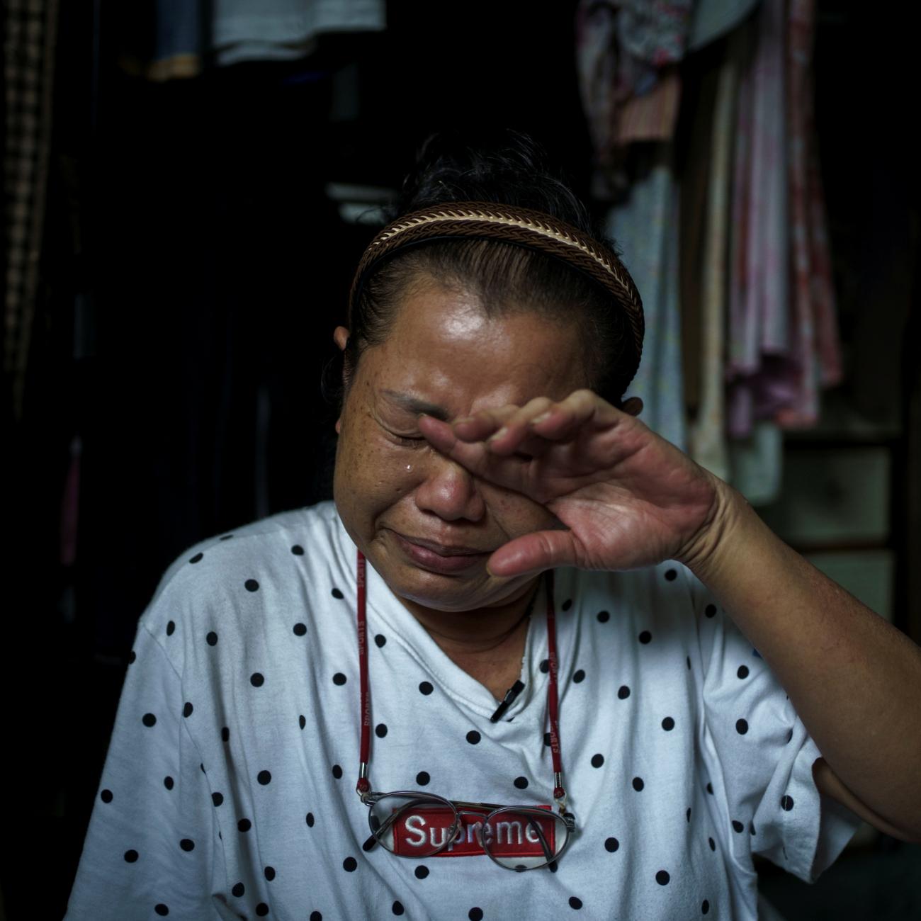 a woman wearing a white patterned t shirt wipes tears off her face