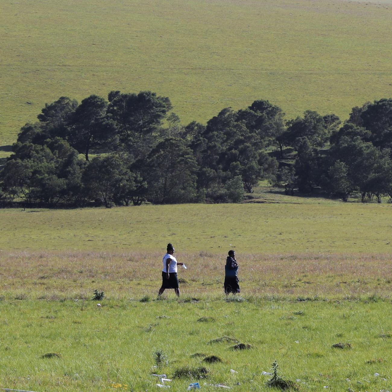 A green field and trees are the backdrop as two women walk, holding a face mask, in Dutywa, in the Eastern Cape province, South Africa, on November 29, 2021. News of the new COVID Omicron variant, now spreading in South Africa, was announced this week.