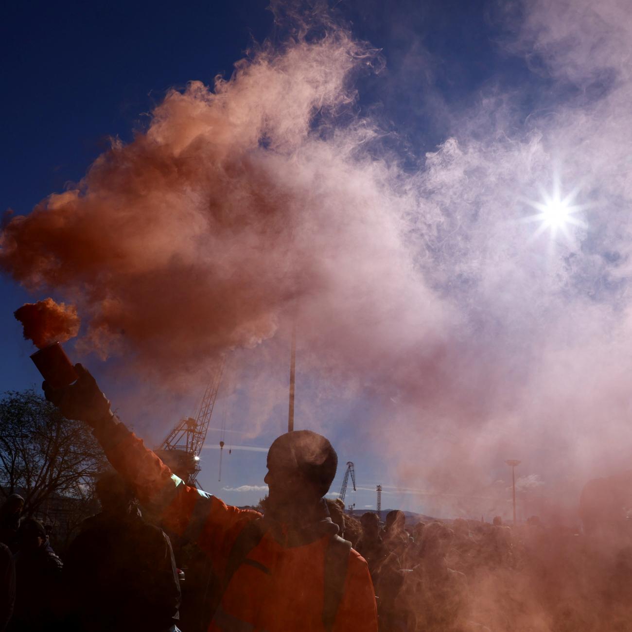 A person holds a flare as port workers gather outside the entrance of the major port of Trieste to protest against the implementation of the COVID-19 health pass, the Green Pass, in the workplace, in Trieste, Italy, October 15, 2021.