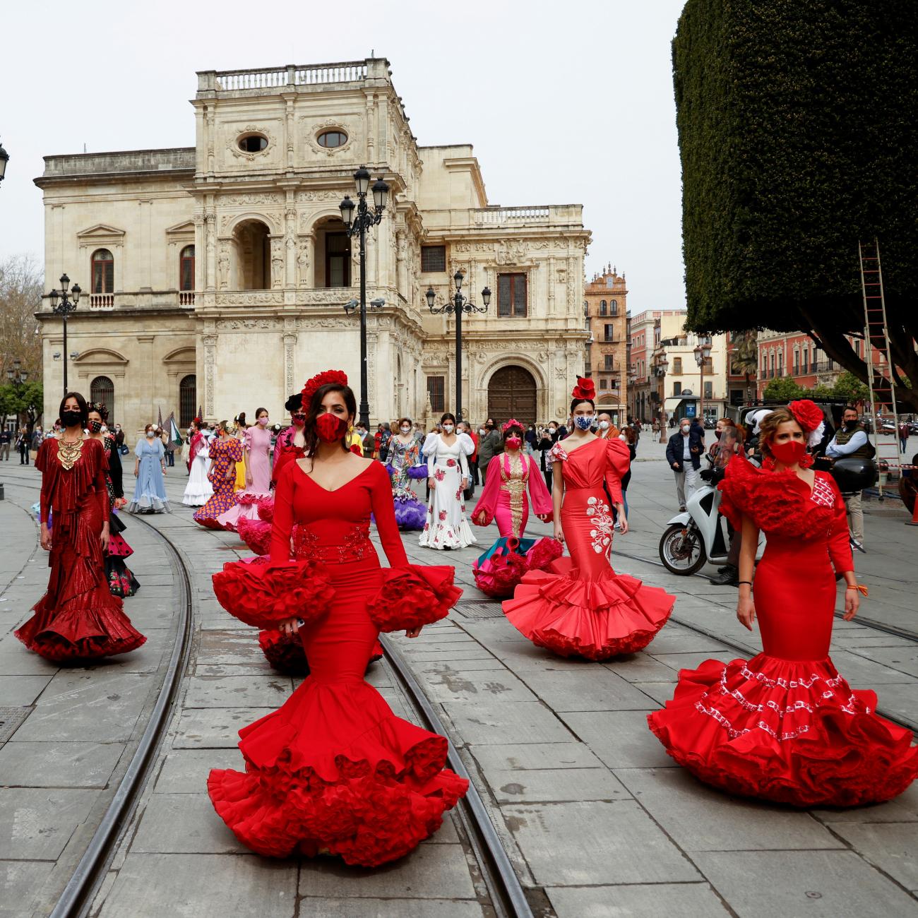 women dressed in traditional flamenco dresses walk in a city square 