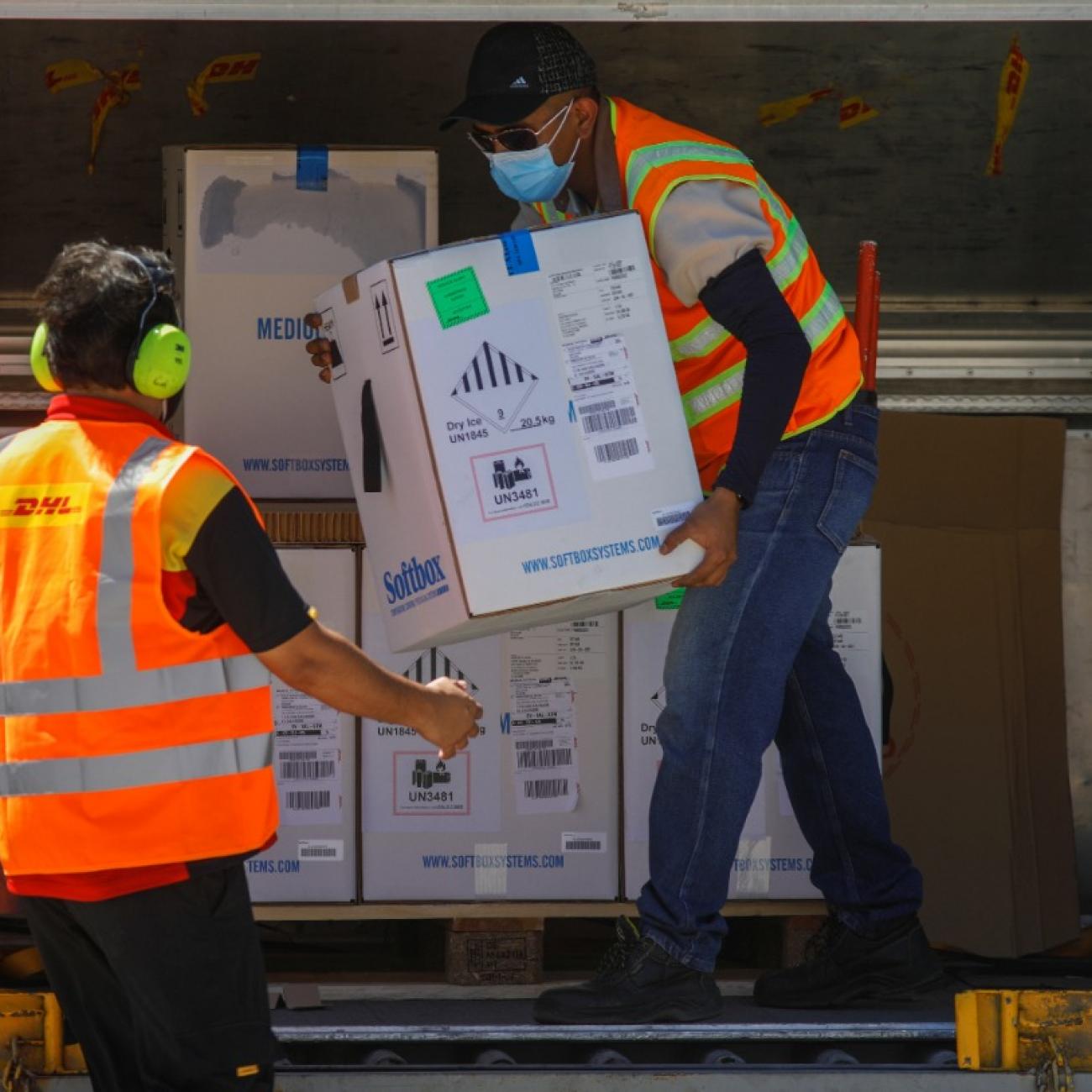 An air carrier worker in an orange vest transfers a box of Pfizer-BioNTech vaccine against the COVID-19 under the COVAX scheme at an airport in San Luis Talpa, El Salvador