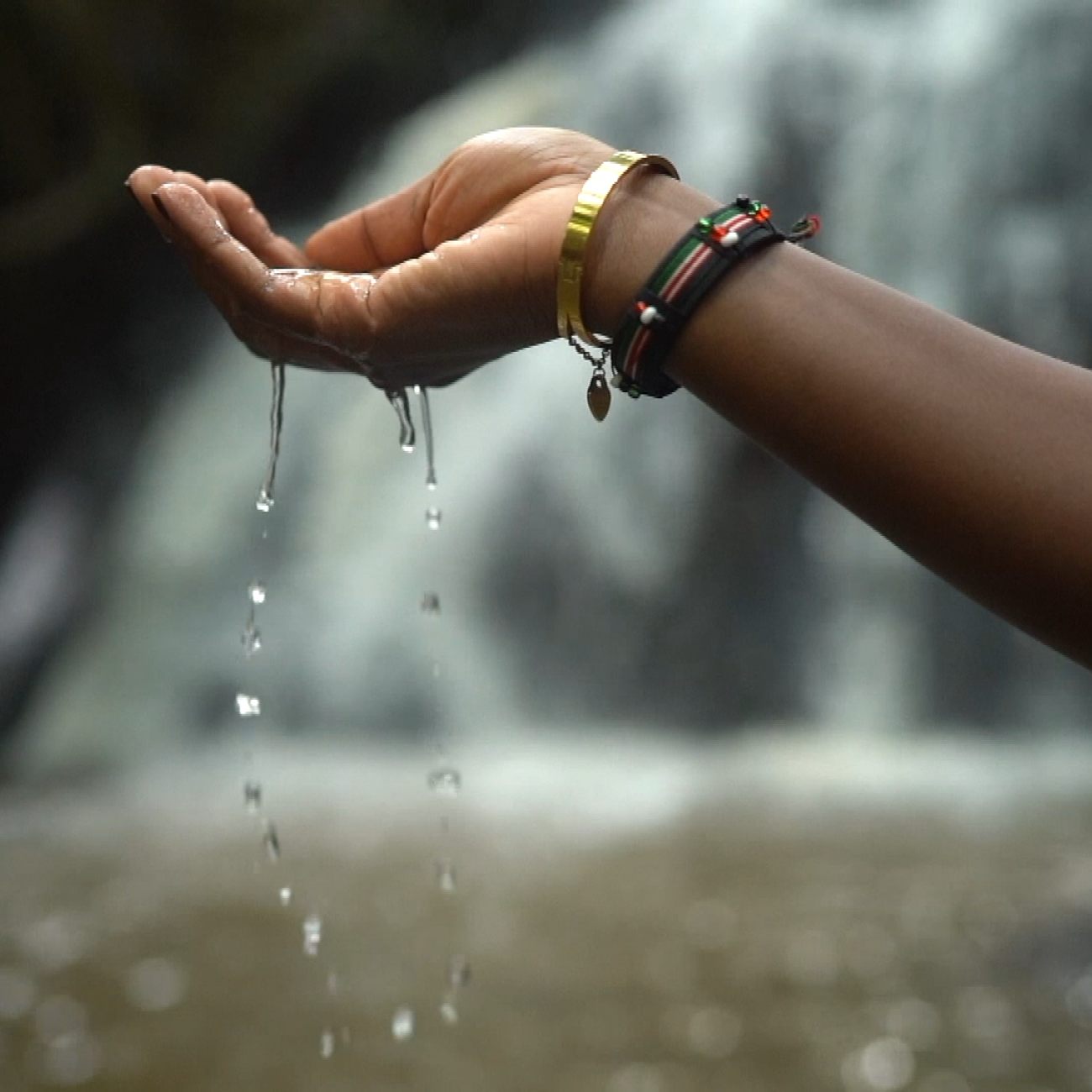 Dr. Liz Wangia lets water from a waterfall trickle from her hand in Nairobi National Park, Kenya