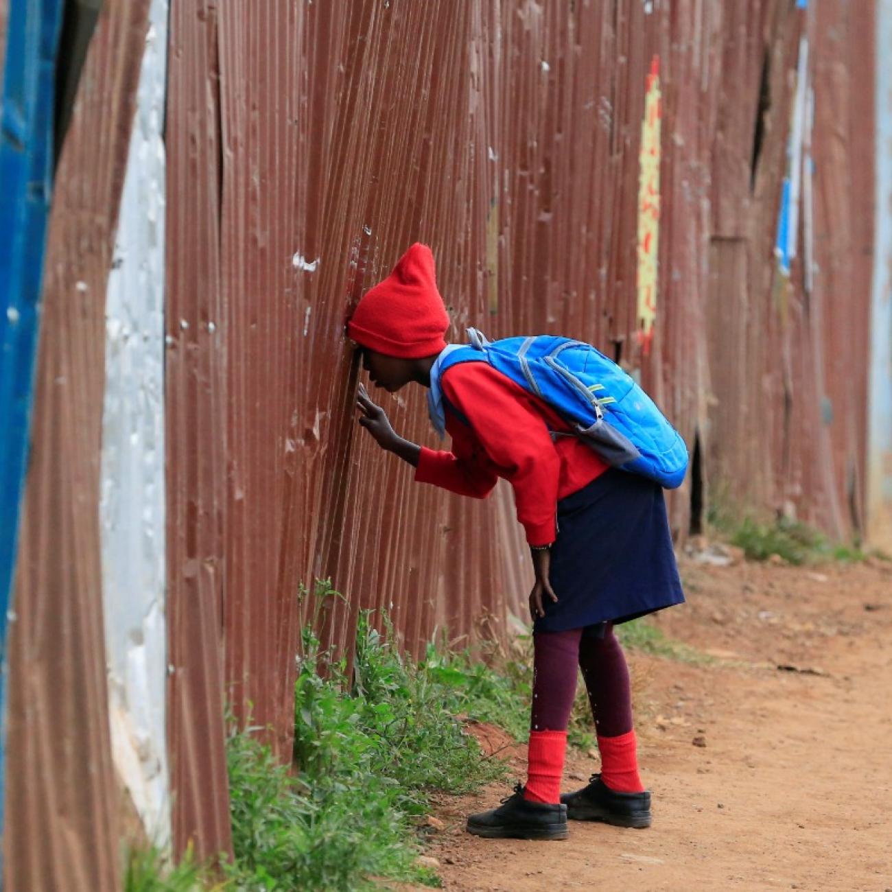 A girl in a red uniform peeks through the fence of her school in Nairobi, Kenya, after the 2021 school year was delayed