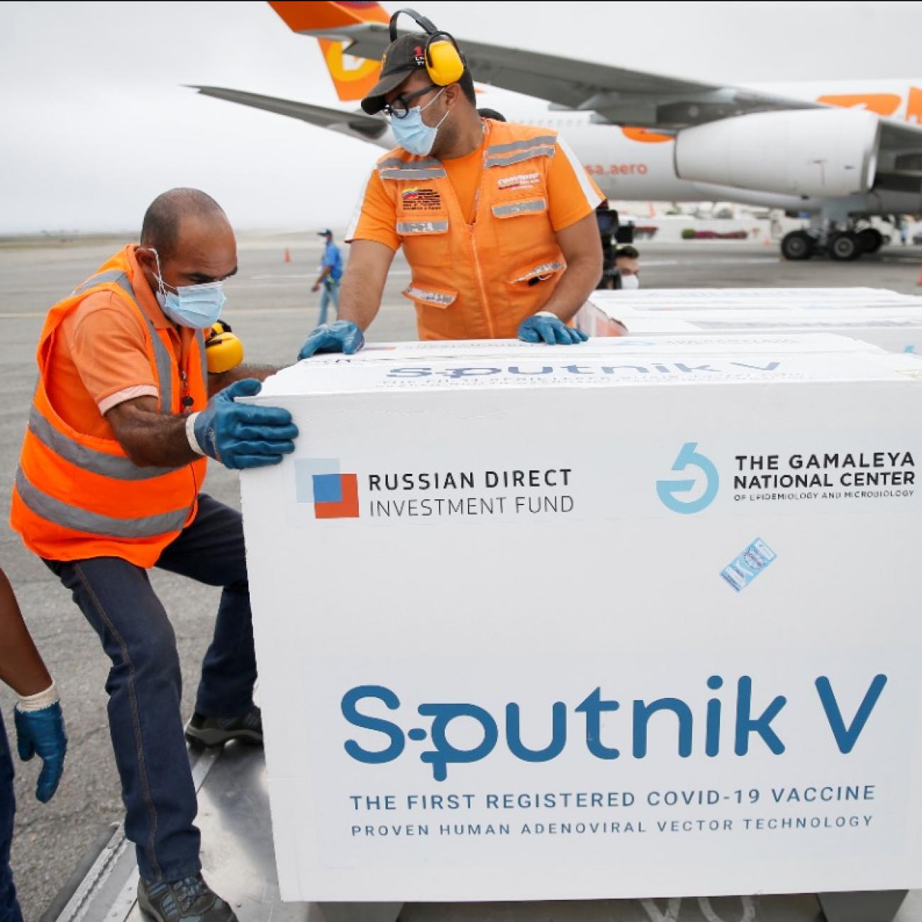 Workers in orange vests unload crates of Sputnik V at an airport in Caracas, Venezuela