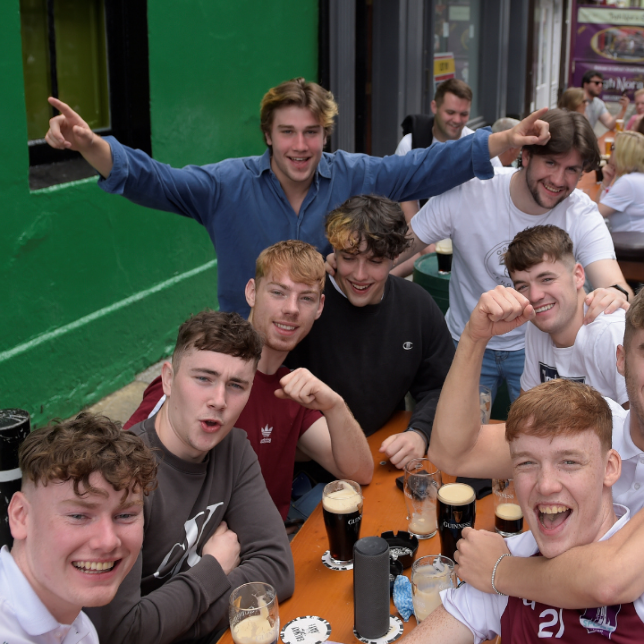 A group of young men cluster around a large outdoor table cheering, smiling, and drinking large glasses of beer as COVID-19 restrictions ease in Galway, Ireland, on June 7, 2021.