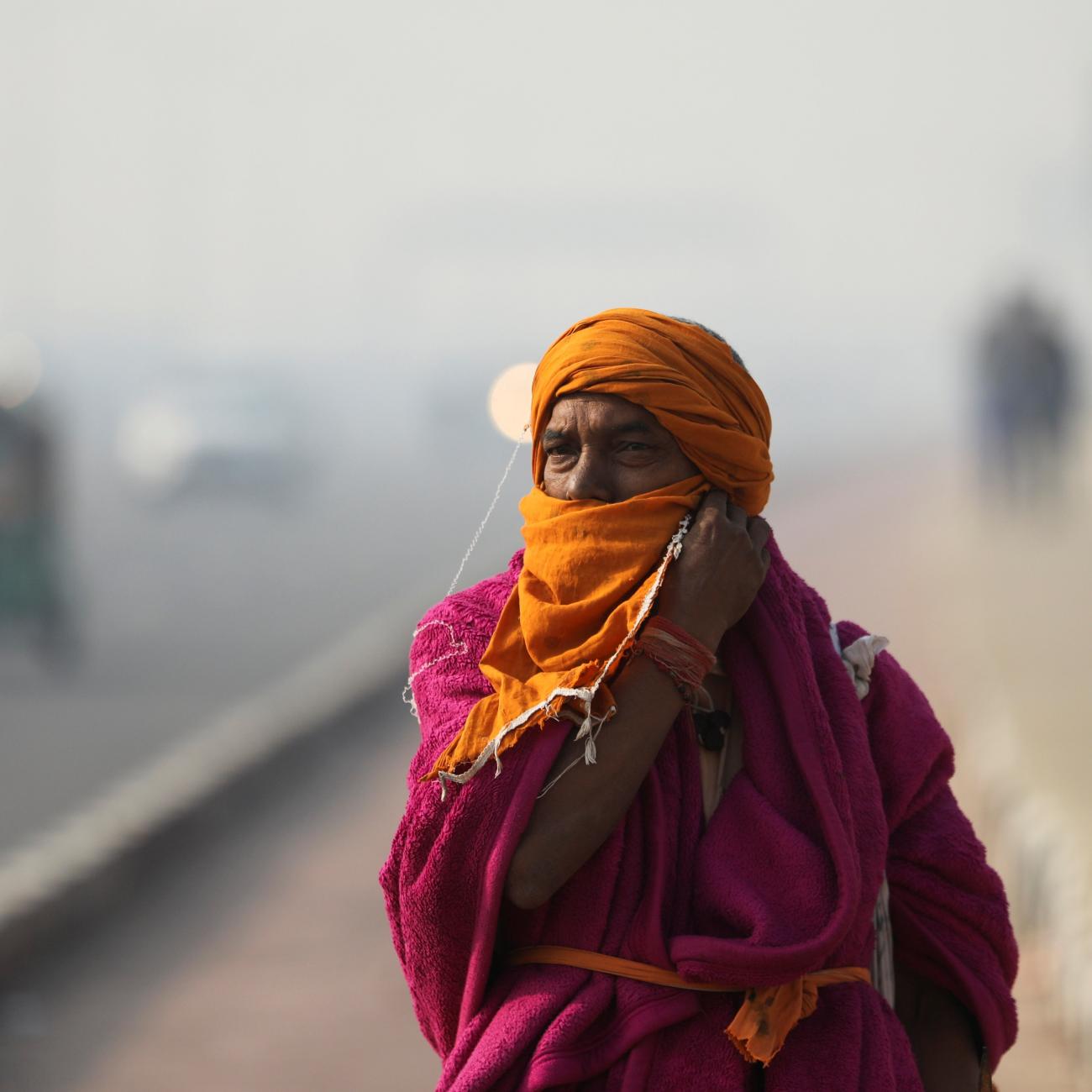 A Sadhu or a Hindu holy man robed in pink and orange adjusts a cloth on his face as he walks across a highway on a smoggy morning in New Delhi, India, November 18, 2021