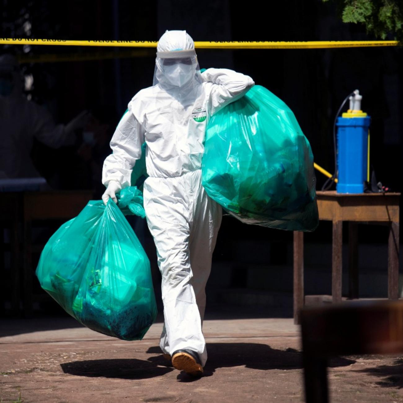 A medical worker carries green plastic bags of medical waste from a quarantine center in Myanmar during the COVIF-19 pandemic