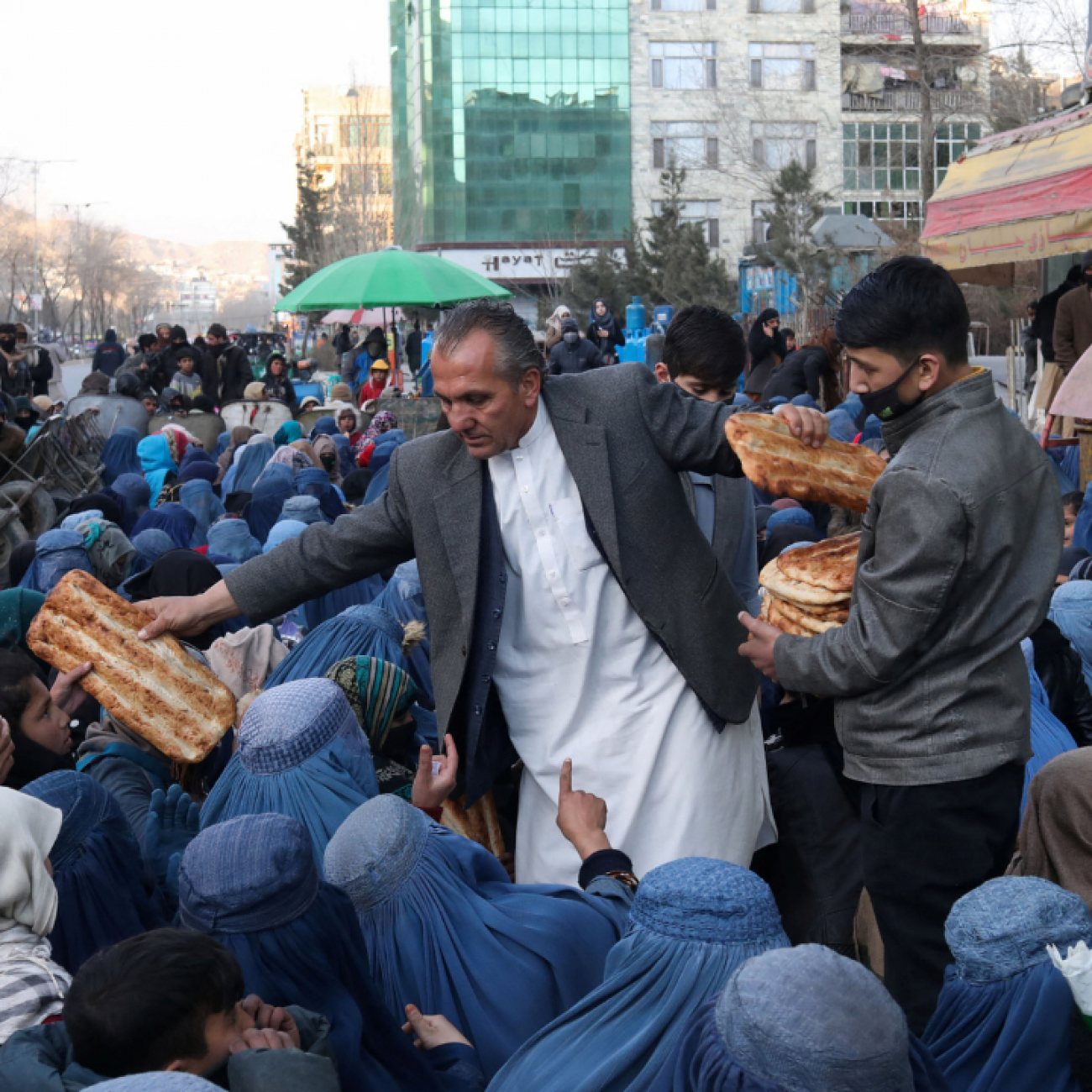 Mehr del Khan Rahmati, who is in charge of a bakery, passes a large flat piece of bread to people awaiting food, in Kabul, Afghanistan, January 31, 2022. 