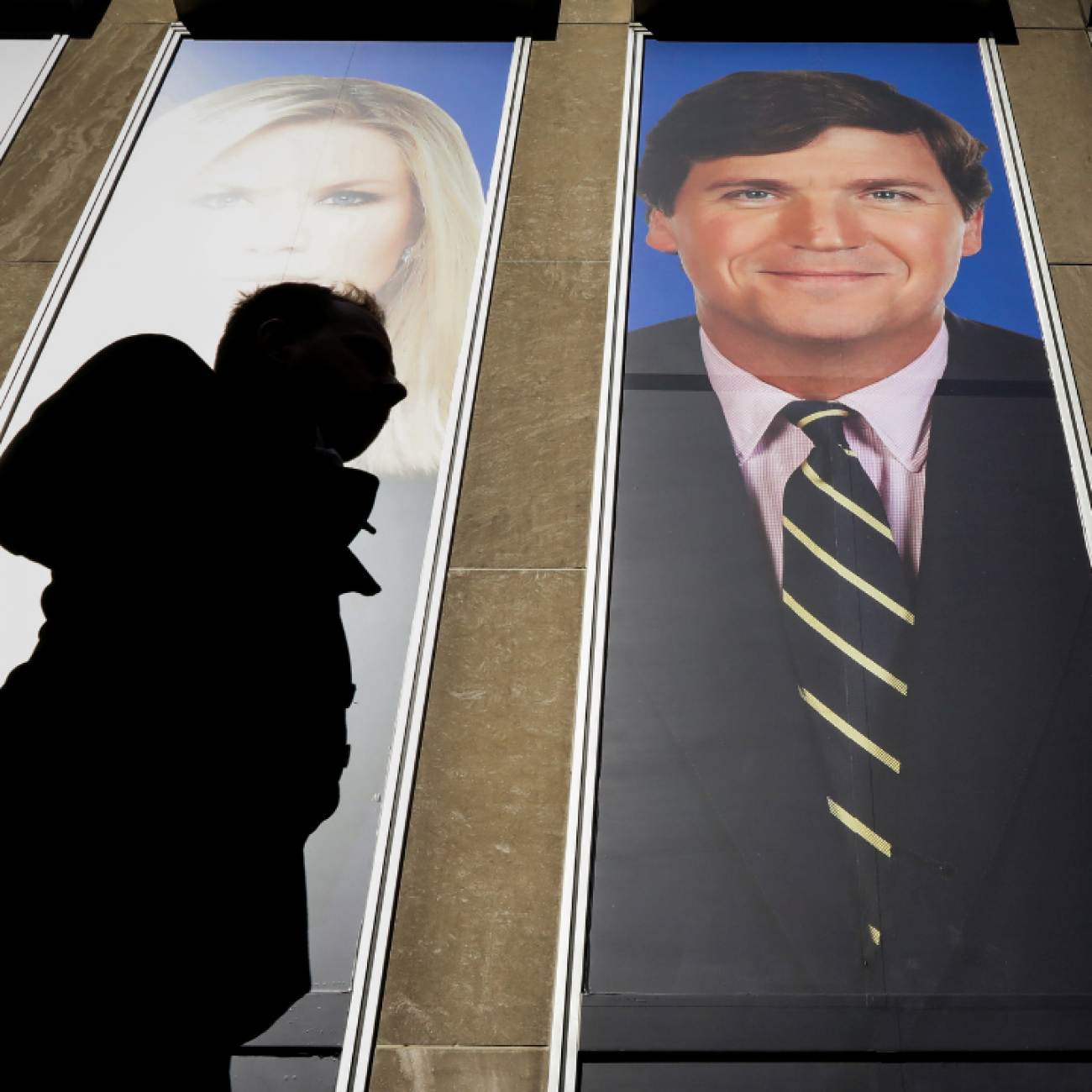 People pass by a promotional image of Fox News' Tucker Carlson on a building in New York, on March 13, 2019.