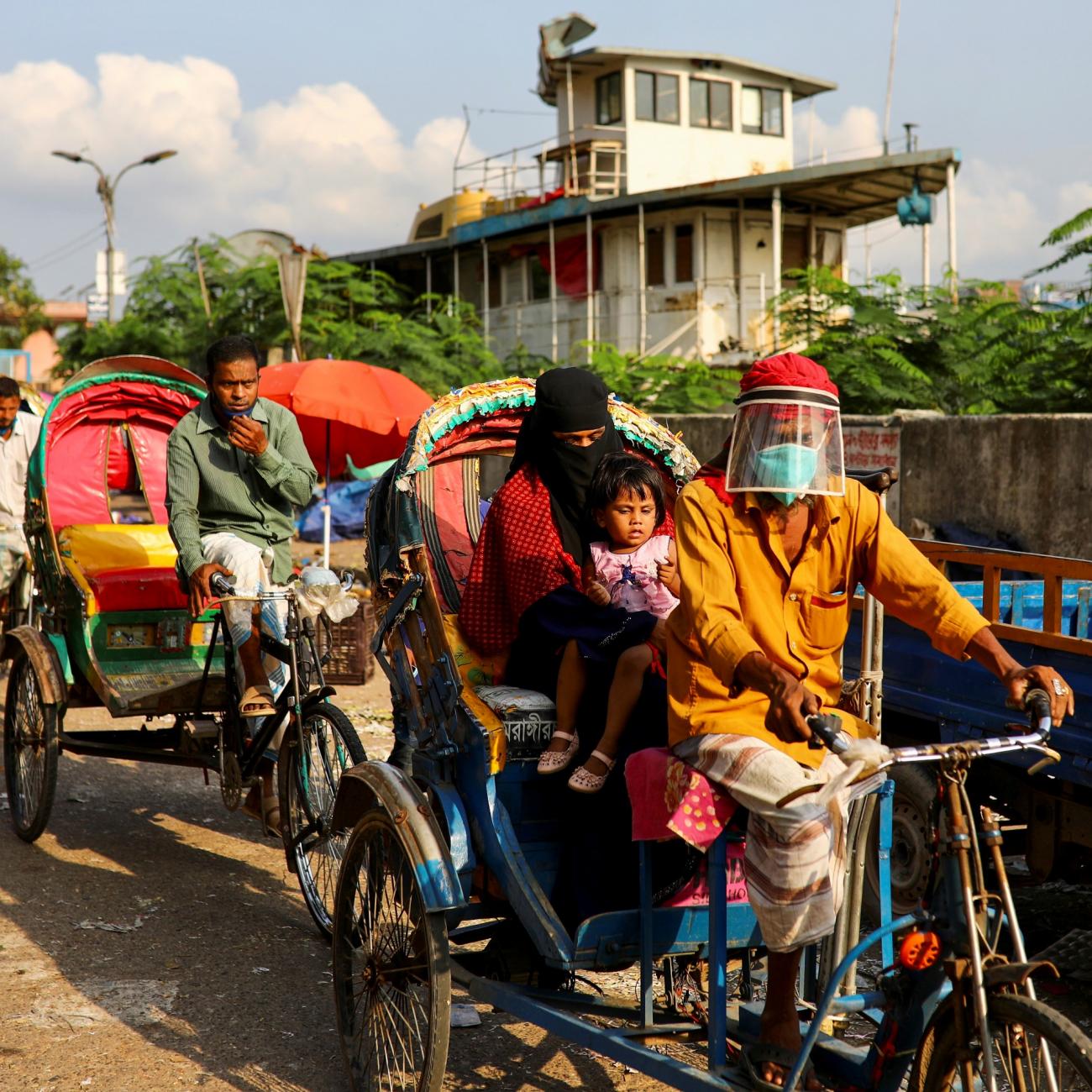 Ricksha pullers wearing face shields and blue medical masks carry passengers in a row rickshas with yellow, orange, and green covers amid the COVID-19 outbreak, in Dhaka, Bangladesh, on June 1, 2020. 