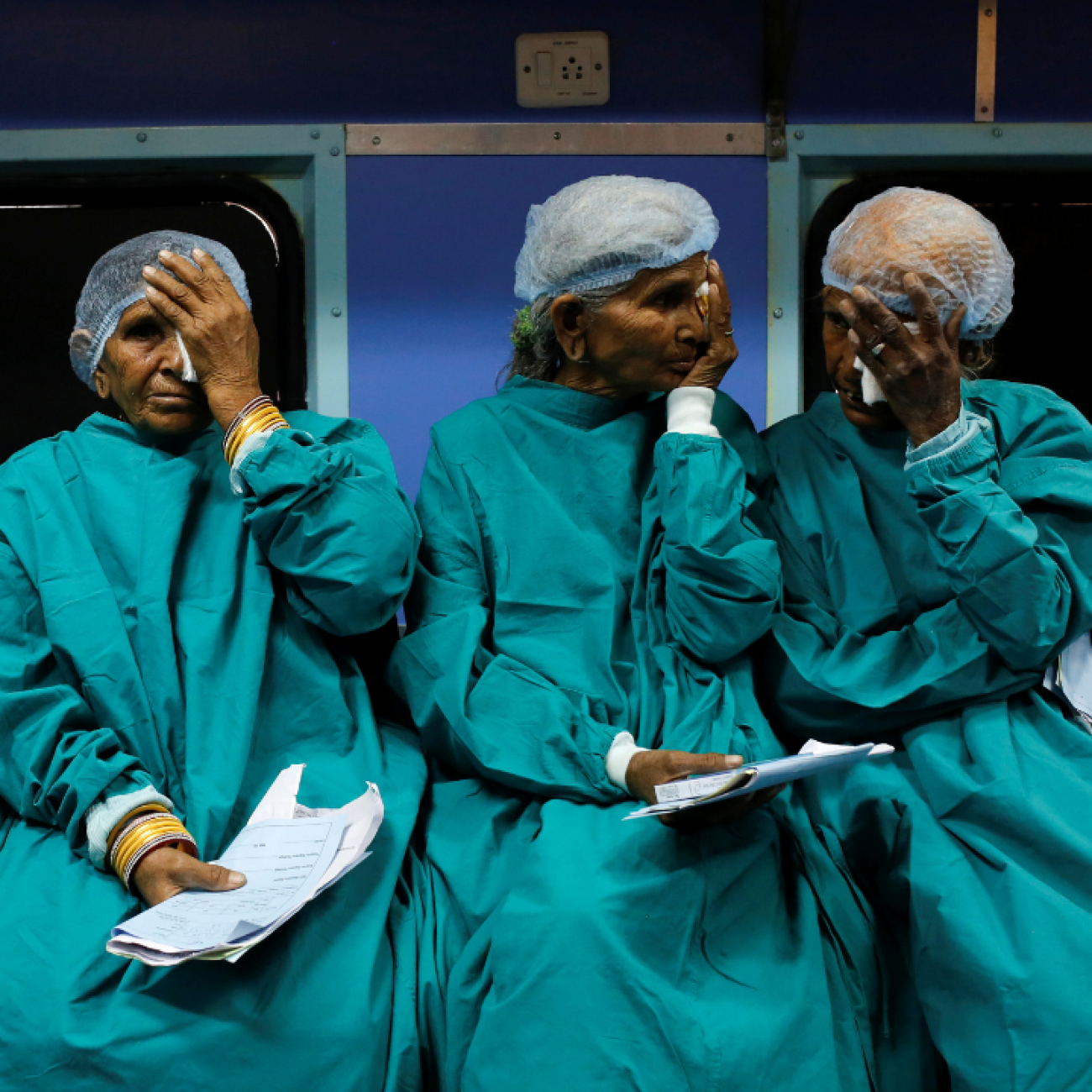 Four older patients dressed in medical gowns cover their eyes as they wait for cataract surgery on the Lifeline Express, a hospital built inside a seven-coach train, at a railway station in Jalore, India, on March 31, 2018. 
