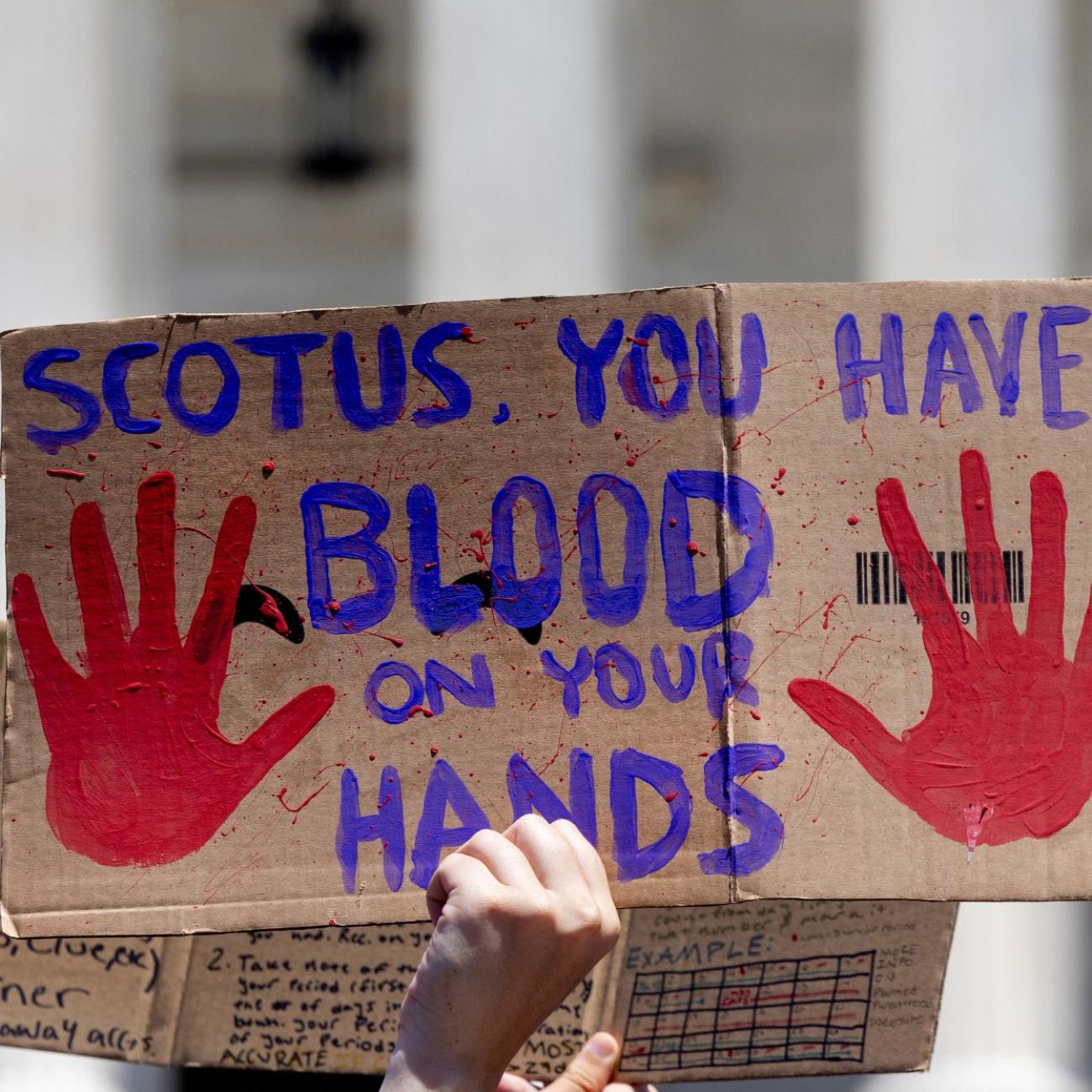 a cardboard signs reads "SCOTUS you have blood on your hands"