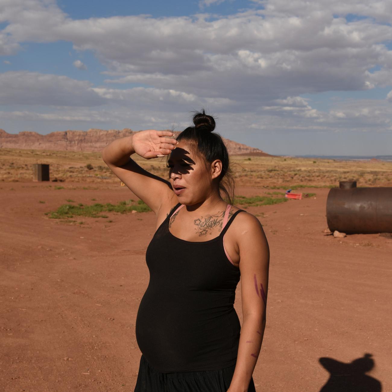 a pregnant woman from the Navajo nation wearing a black tank top shields her eyes from the sun
