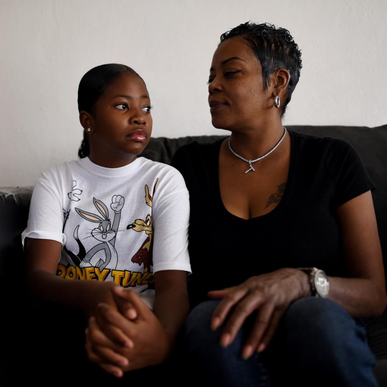 a girl in a white t shirt sits next her mom wearing a black shirt on a tattered couch