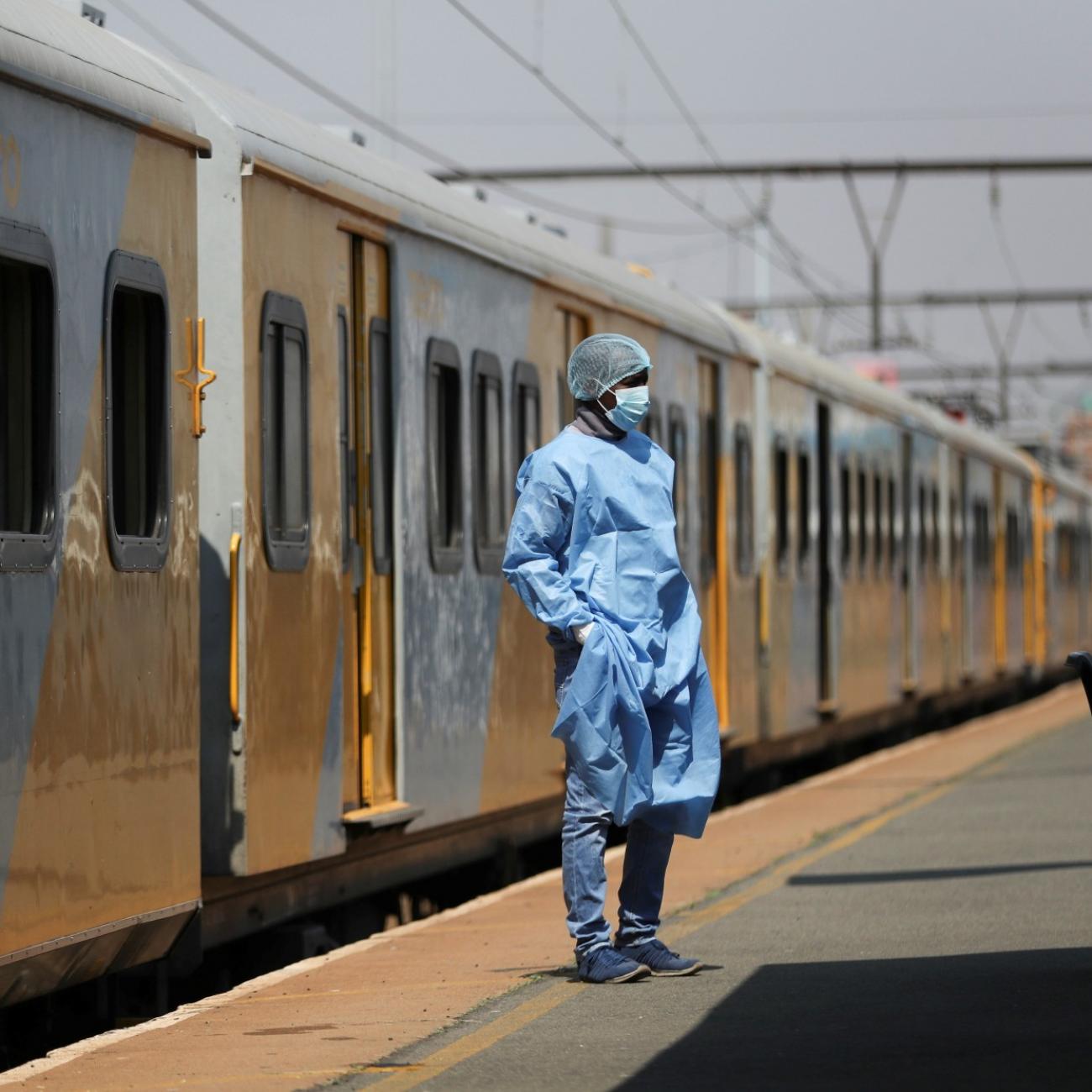 a health-care worker in blue scrubs and PPE stands in front of a train car