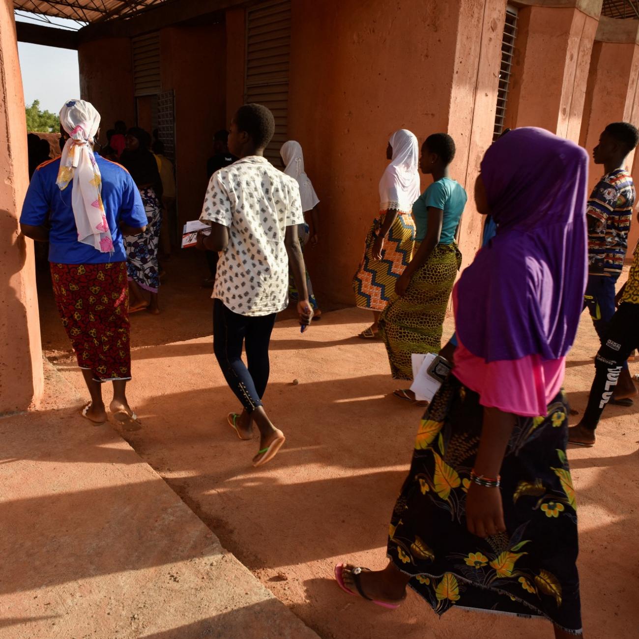 students wearing colorful clothing enter a terracotta colored building in Kenya