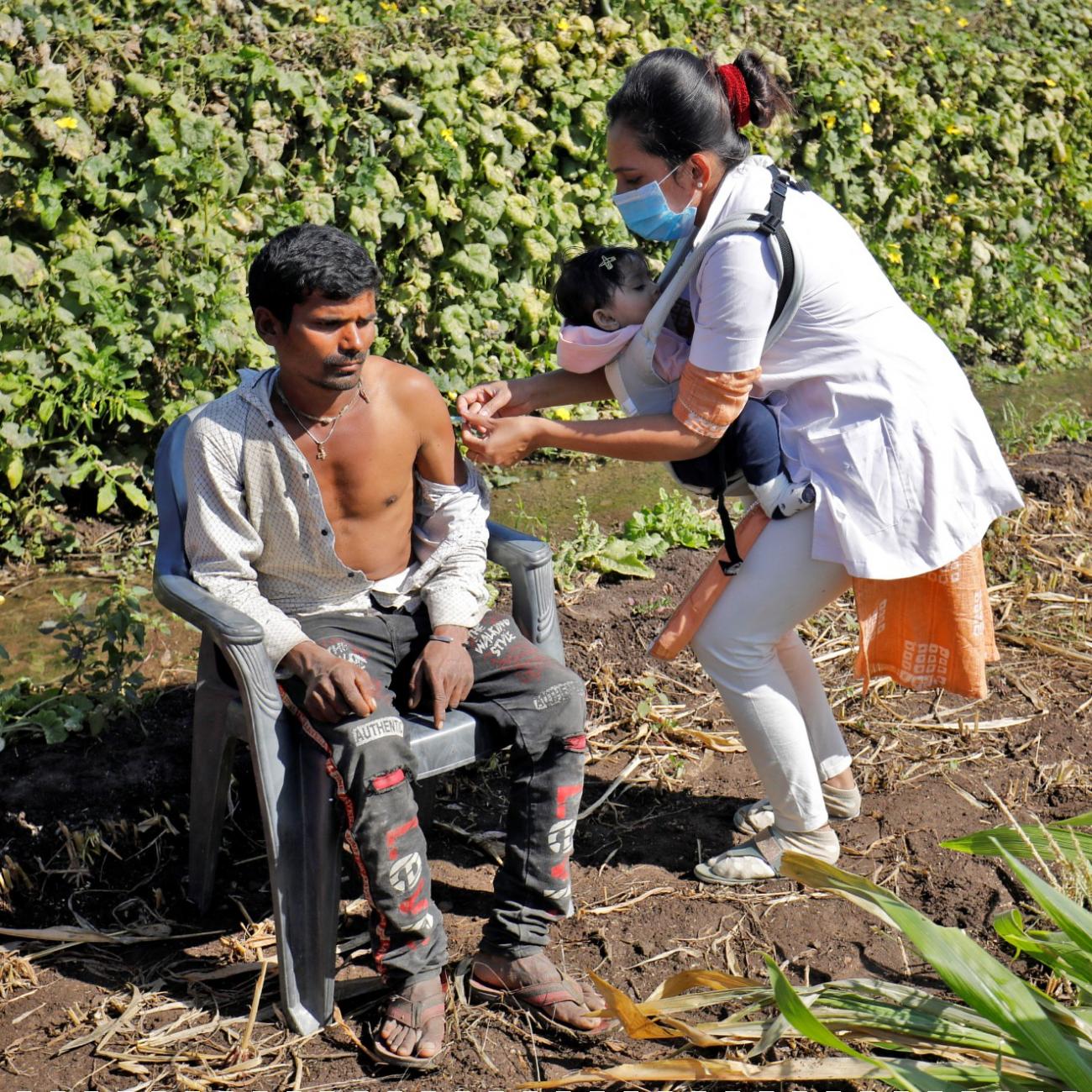 Asmita Koladiya, a health-care worker, carrying her eight-month-old daughter, gives a dose of vaccine against COVID-19 to a man in Lodhida village, in Gujarat, India, on February 2, 2022.