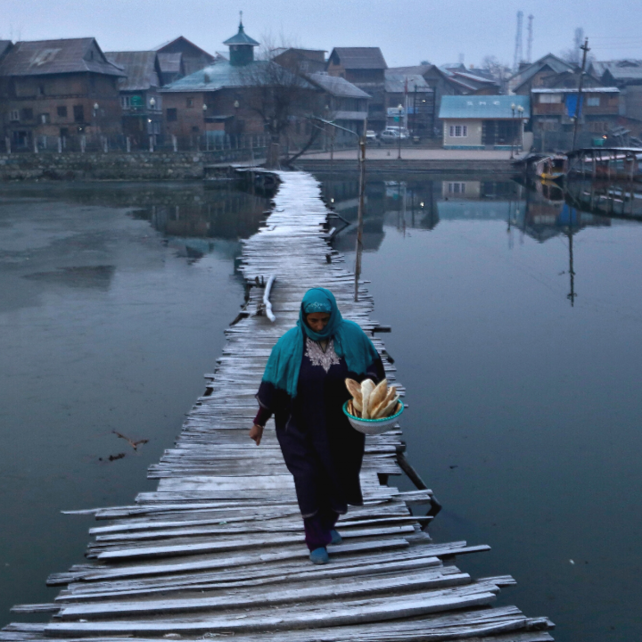 A woman dressed in a head covering and long dress carries bread as she walks on a frost-covered footbridge in the interiors of Nigeen Lake on a cold winter morning in Srinagar, India, December 24, 2020. REUTERS/Danish Ismail