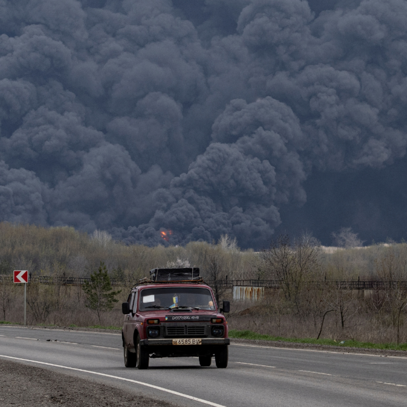 Plumes of black smoke rise up into the air behind a car as it passes the Lysychansk Oil Refinery after if was hit by a missile at Lysychansk, in the Luhansk region, Ukraine, on April 16, 2022. REUTERS/Marko Djurica