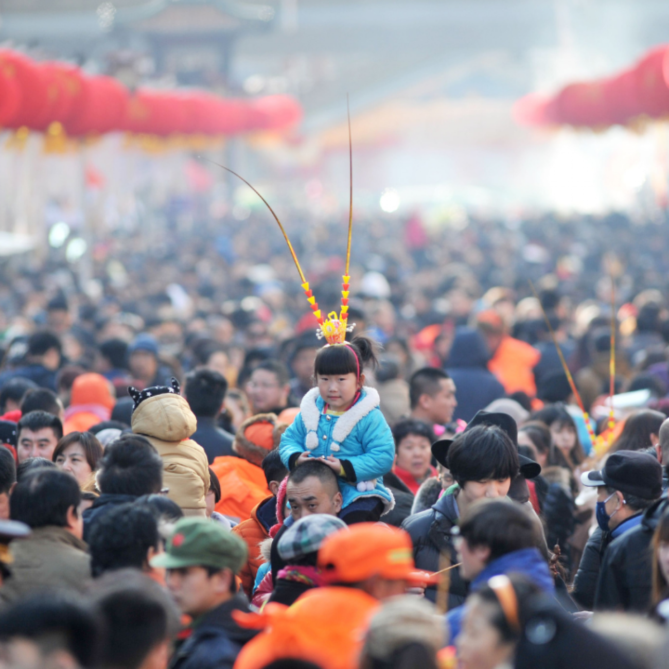 A girl wears a monkey king headwear as she sits on an adult's shouulders above a large crowd at a festival fair during Chinese Lunar New Year celebrations in Qingdao.