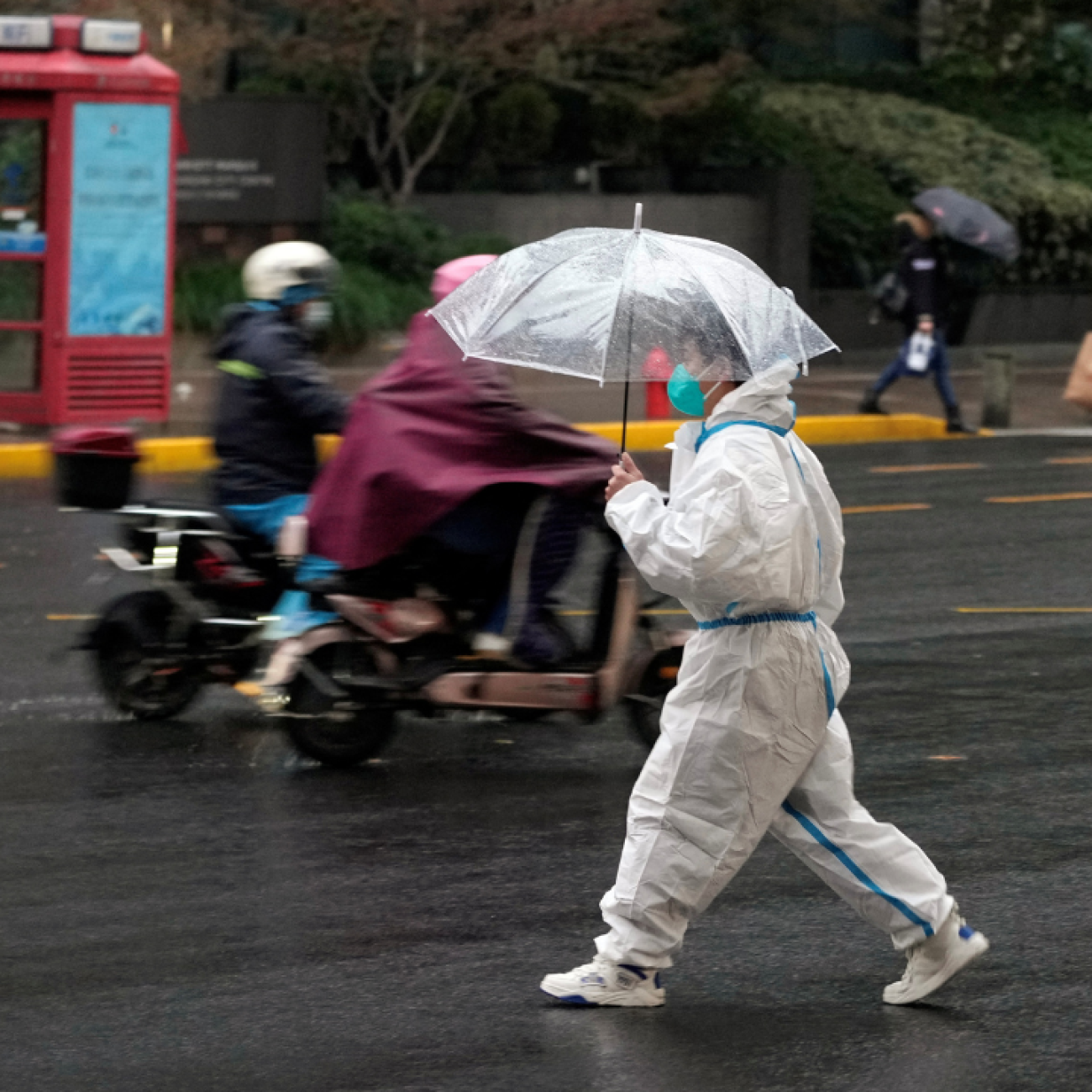 a worker in white protective suit holding an umbrella crosses a road in the rain during a COVID-19 outbreak in Shanghai, China, on November 30, 2022.