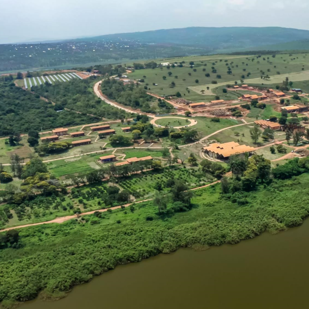 An aerial view of the green campus with earth-colored buildings alongside a river