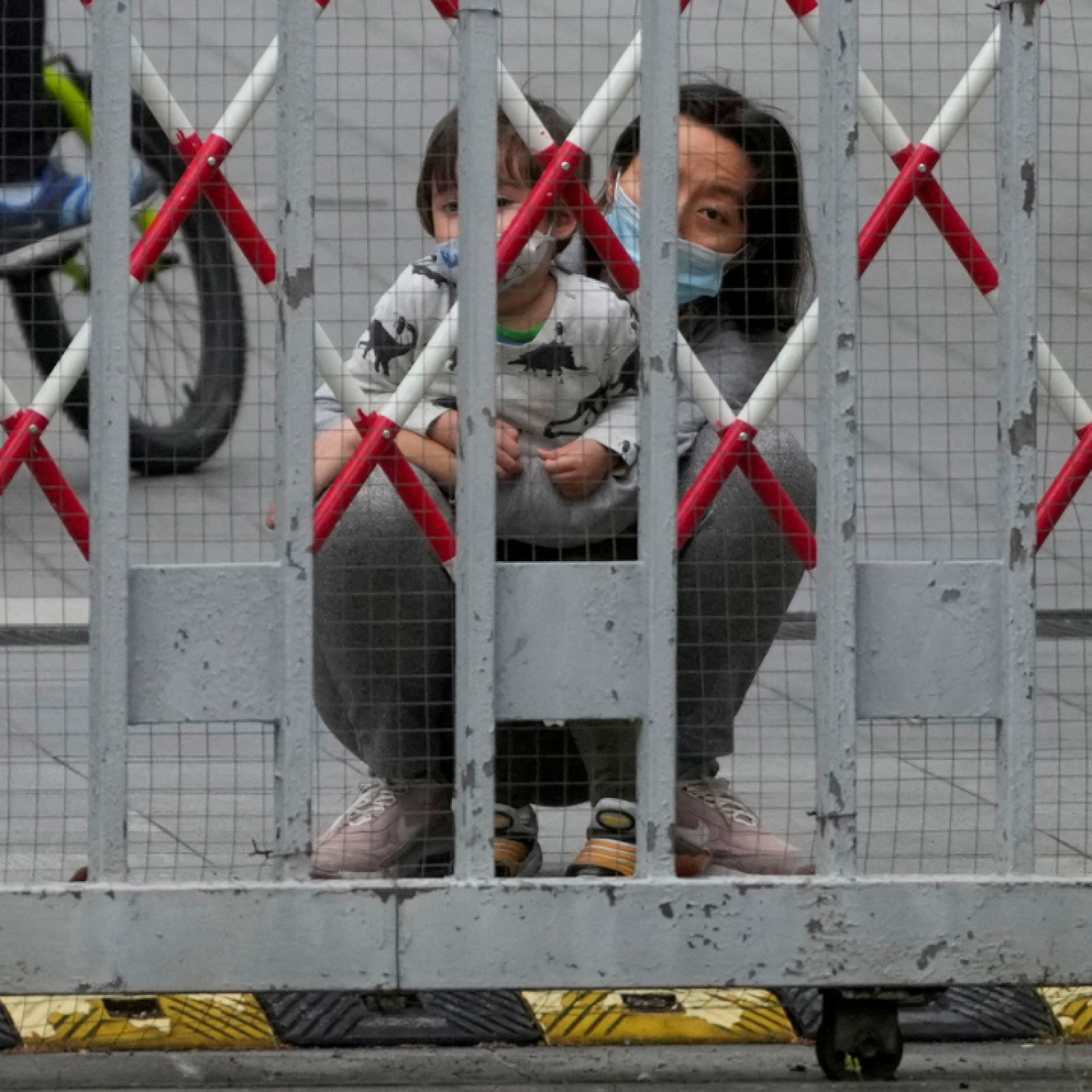 A resident and a child look out through gaps in barriers at a closed residential area during COVID-19 lockdown in Shanghai, China, on May 10, 2022. 