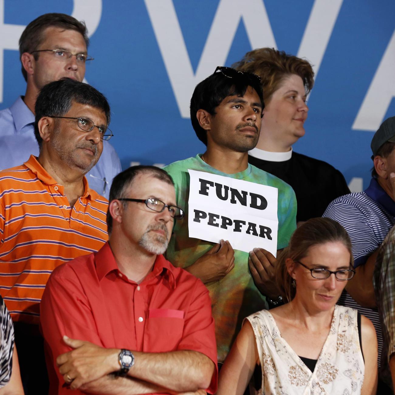 An audience member holds up a "Fund PEPFAR" sign, during President Barack Obama's speech at a campaign event at Herman Park in Boone, Iowa, on August 13, 2012. 