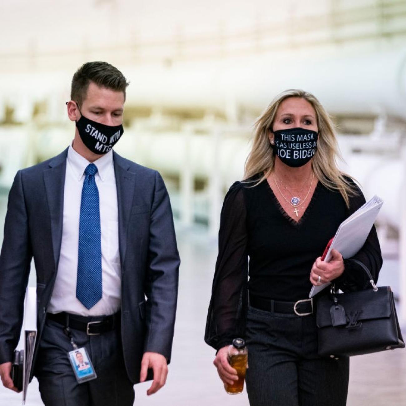Rep. Marjorie Taylor Greene (R-GA) wears a protective mask bearing the words "This mask is as useless as Joe Biden," as she walks with an aide to a vote in the Cannon Tunnell on Capitol Hill, in Washi