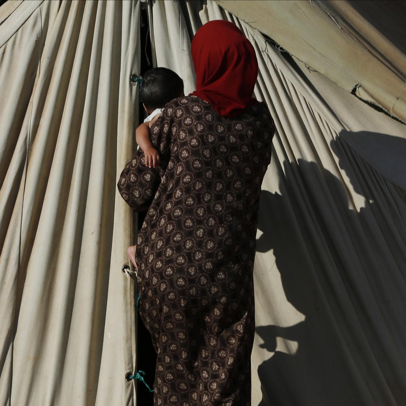 A Syrian refugee from Damascus, carries a child as she enters her tent, at the Majdal Anjar refugee camp in Bekaa Valley near the Syrian border in eastern Lebanon, on September 9, 2013.