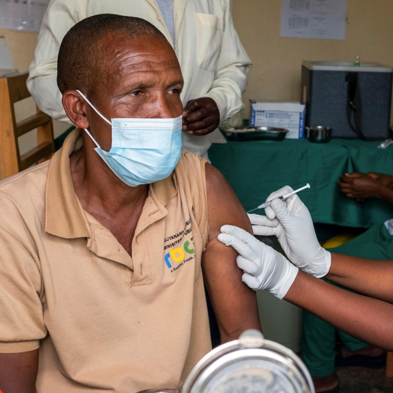 a man wearing a blue surgical mask receives a covid vaccination from a female nurse