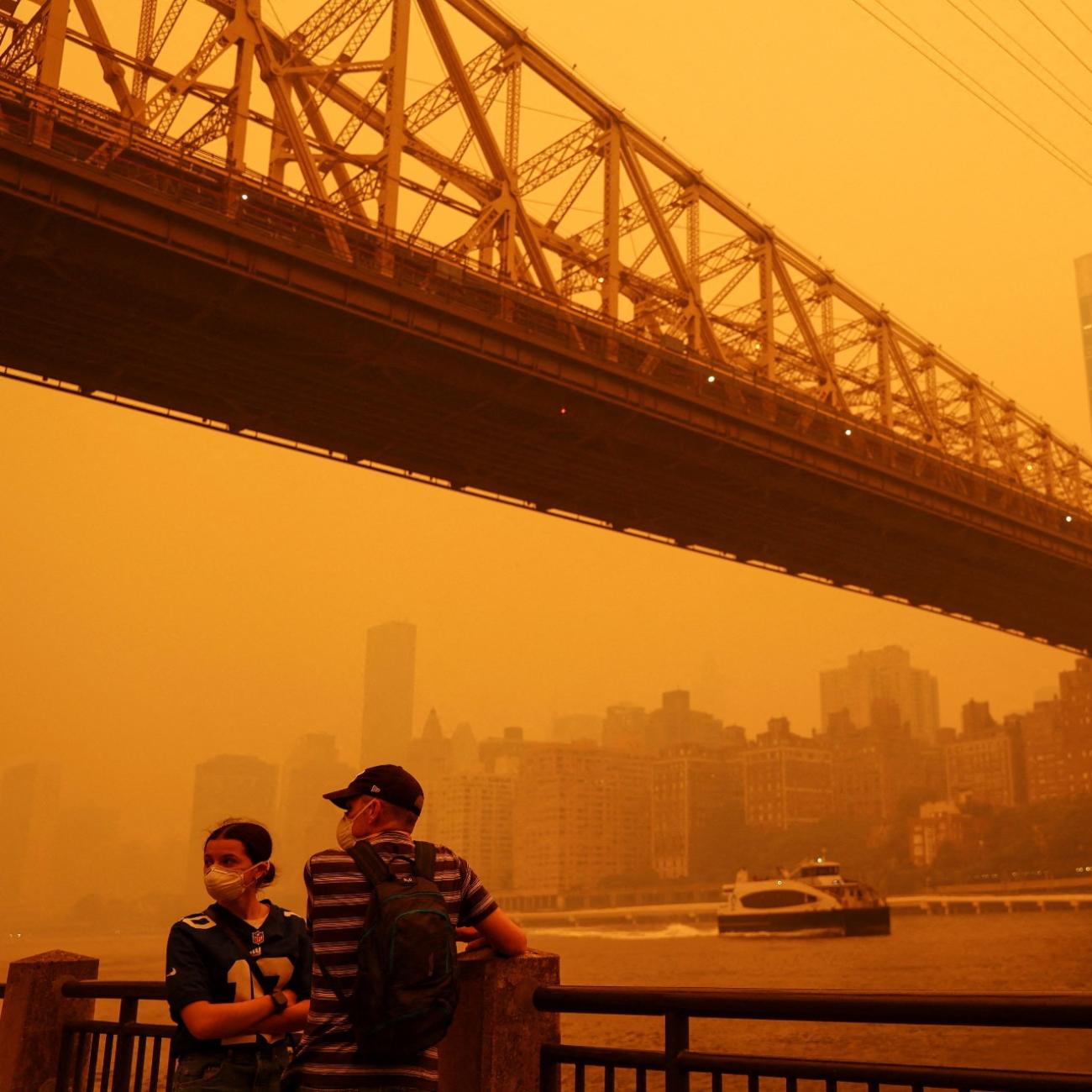 People wear protective masks as the Roosevelt Island Tram crosses the East River while haze and smoke from the Canadian wildfires shroud the Manhattan skyline in the Queens Borough New York City, U.S., June 7, 2023.People wear protective masks as the Roosevelt Island Tram crosses the East River while haze and smoke from Canadian wildfires shroud the Manhattan skyline, in Queens, New York City, on June 7, 2023. 