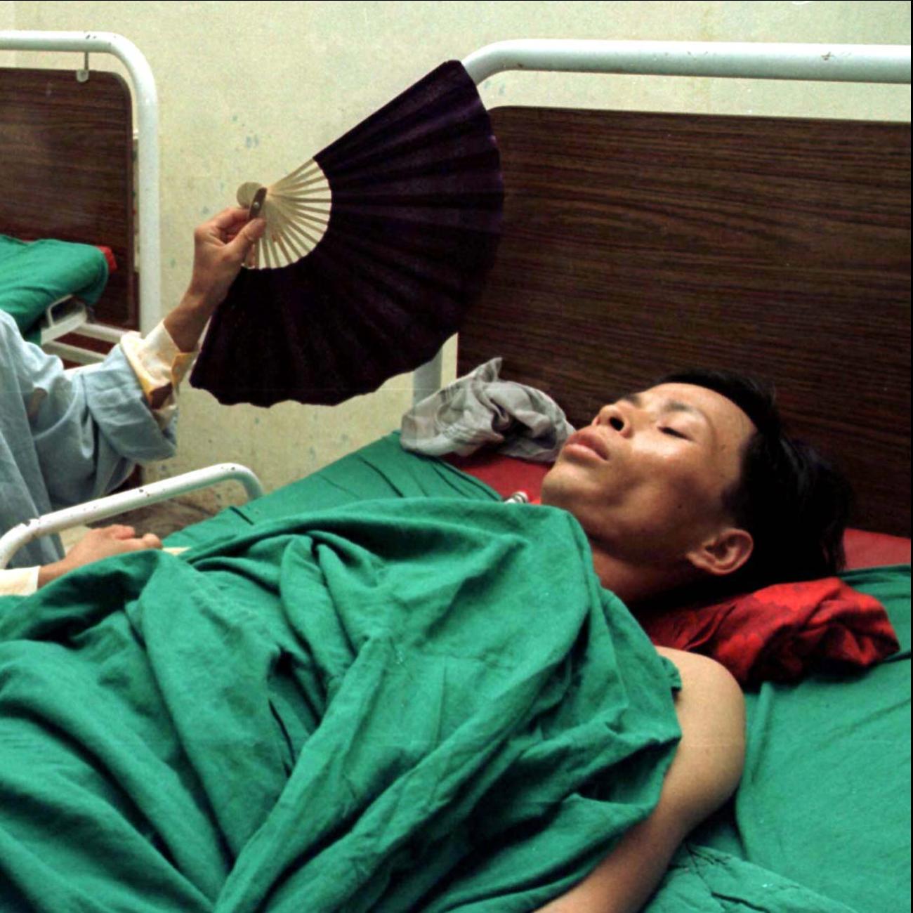 A man is fanned by his wife in the post-operative ward at Institute of Tuberculosis and Respiratory Diseases, after a lung operation for complications caused by tuberculosis, in Hanoi, Vietnam.