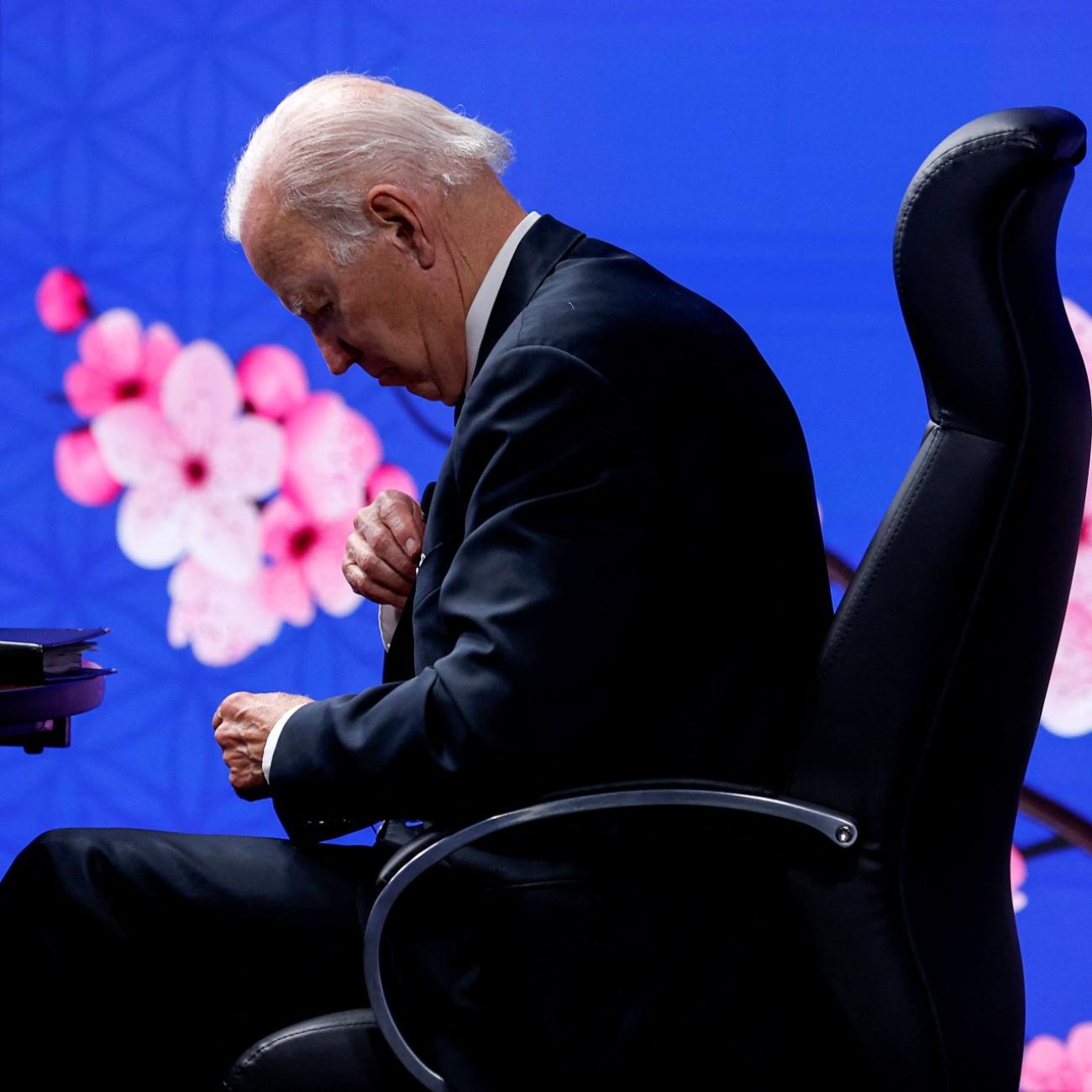 President Biden slouches over in a chair over a cherry blossom screen