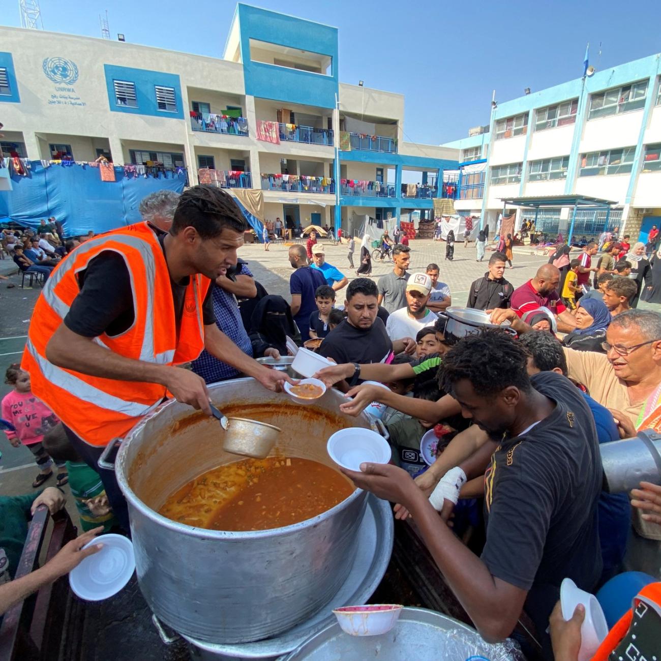 Palestinians, who fled their houses due to Israeli strikes, gather to get their share of charity food