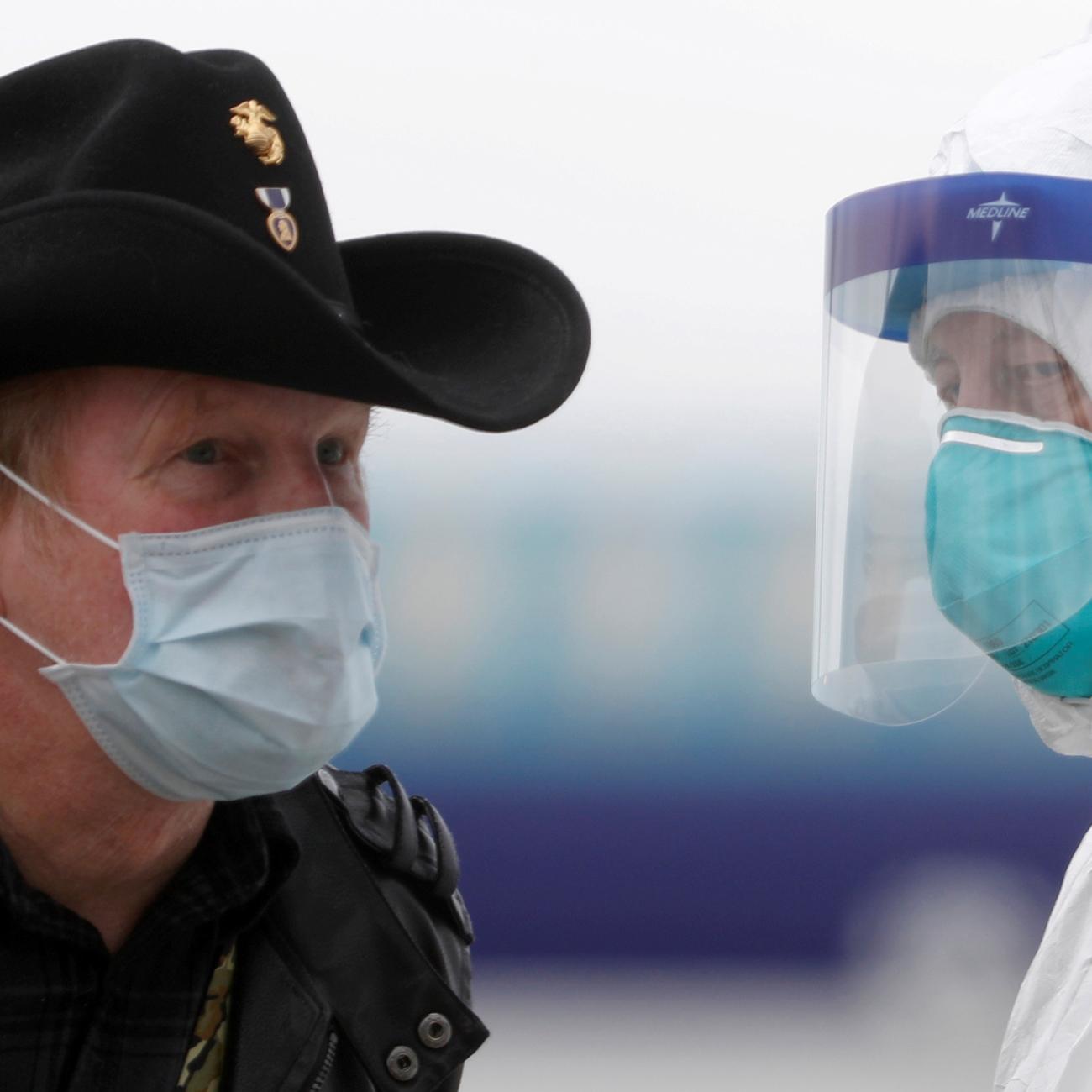 A worker in protective gear directs a masked passenger disembarking from the cruise ship Grand Princess in Oakland, California on March 10, 2020 amid concern over the growing COVID-19 pandemic. The picture shows a man wearing a mask and a cowboy hat standing facing a health worker in full protective gear. REUTERS/Stephen Lam 