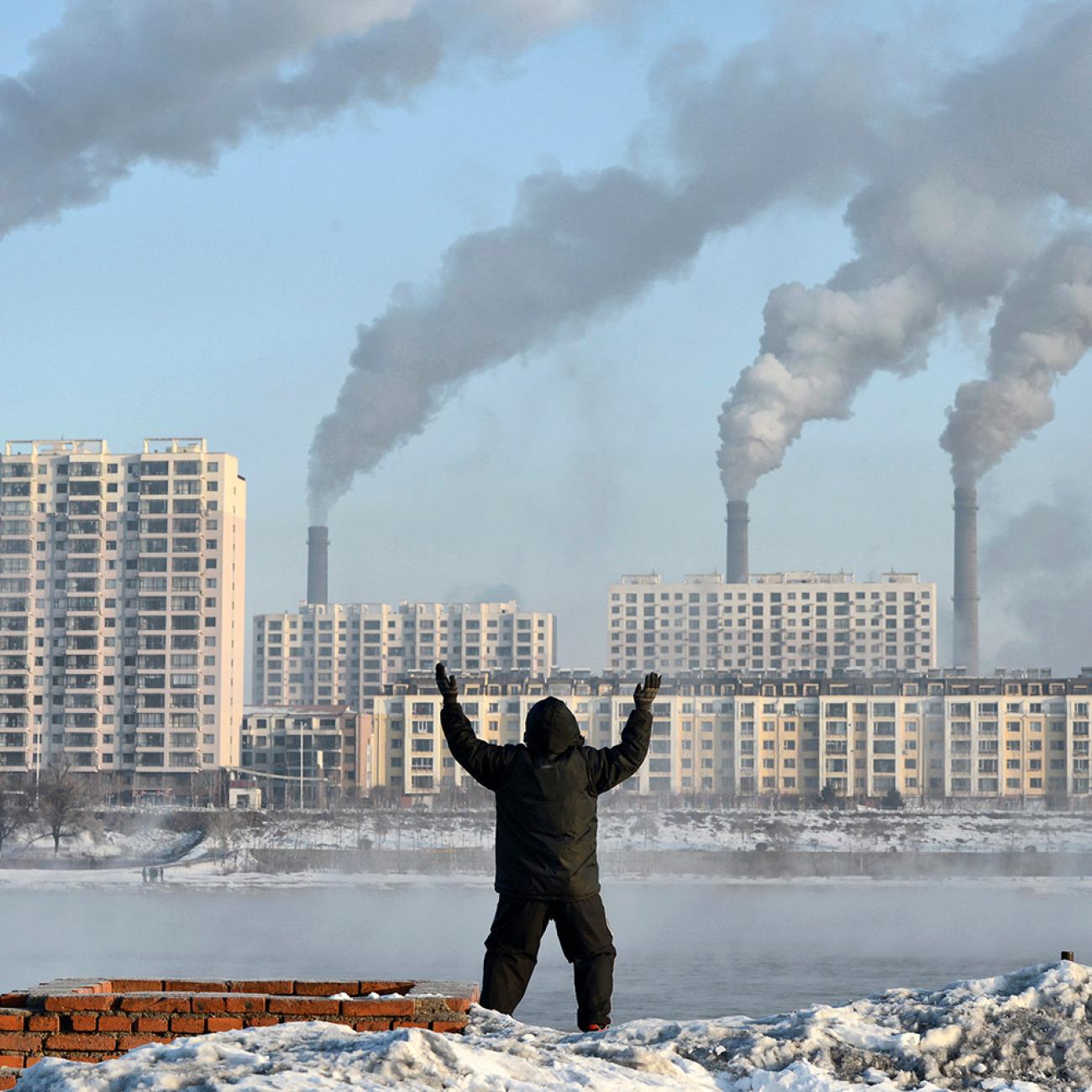 Factories emit smoke in Jilin province, China, across the Songhua River from where an elderly man exercises on the morning of Feb 24, 2013, after Chinese authorities announced plans to curb pollution. The photo shows the man in the foreground, back to the camera, with buildings on the other side of the river pouring out smoke. REUTERS/Stringer