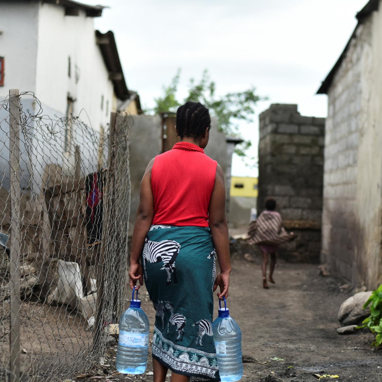 A woman carries bottles of water in a neighborhood affected by the cholera outbreak.