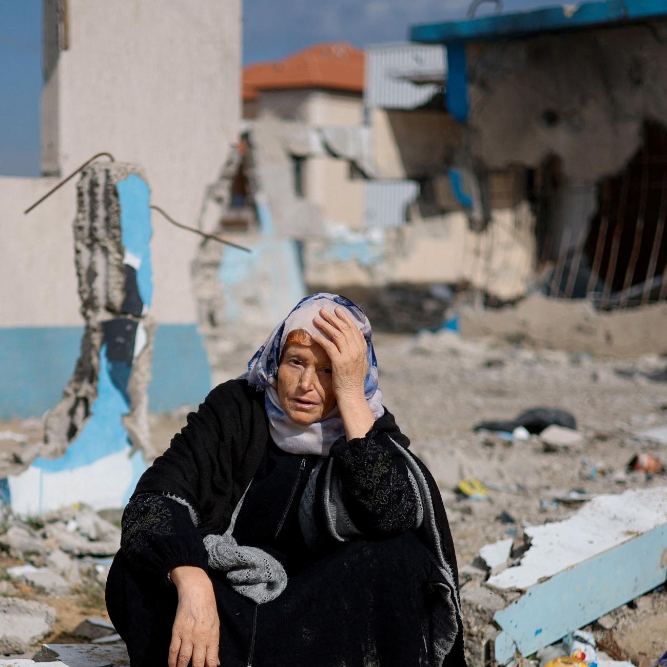 A woman rests next to a damaged building, as Palestinian arrive in Rafah after they were evacuated from Nasser hospital in Khan Younis.