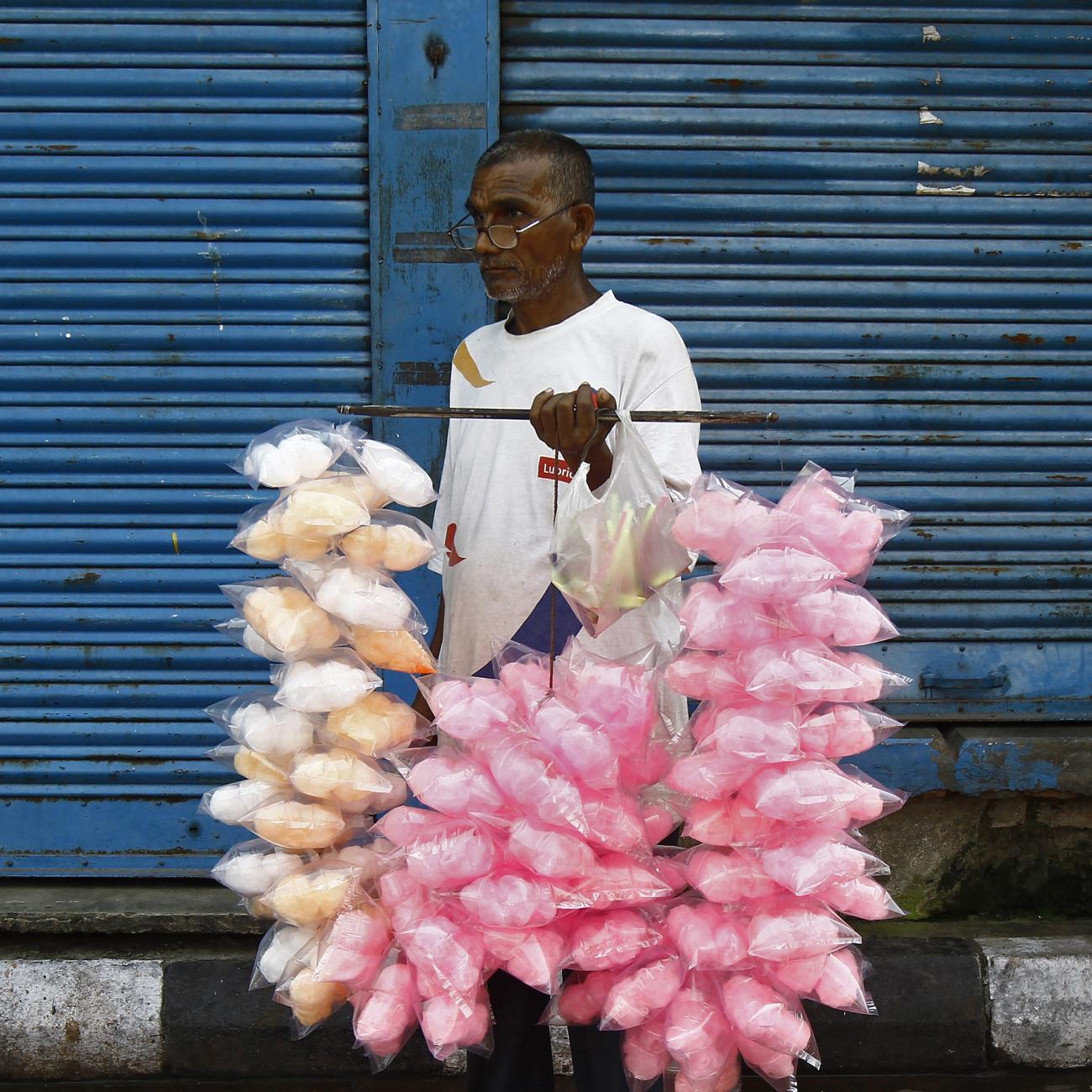 A vendor selling candy floss stands in front of closed shops along the roadside.