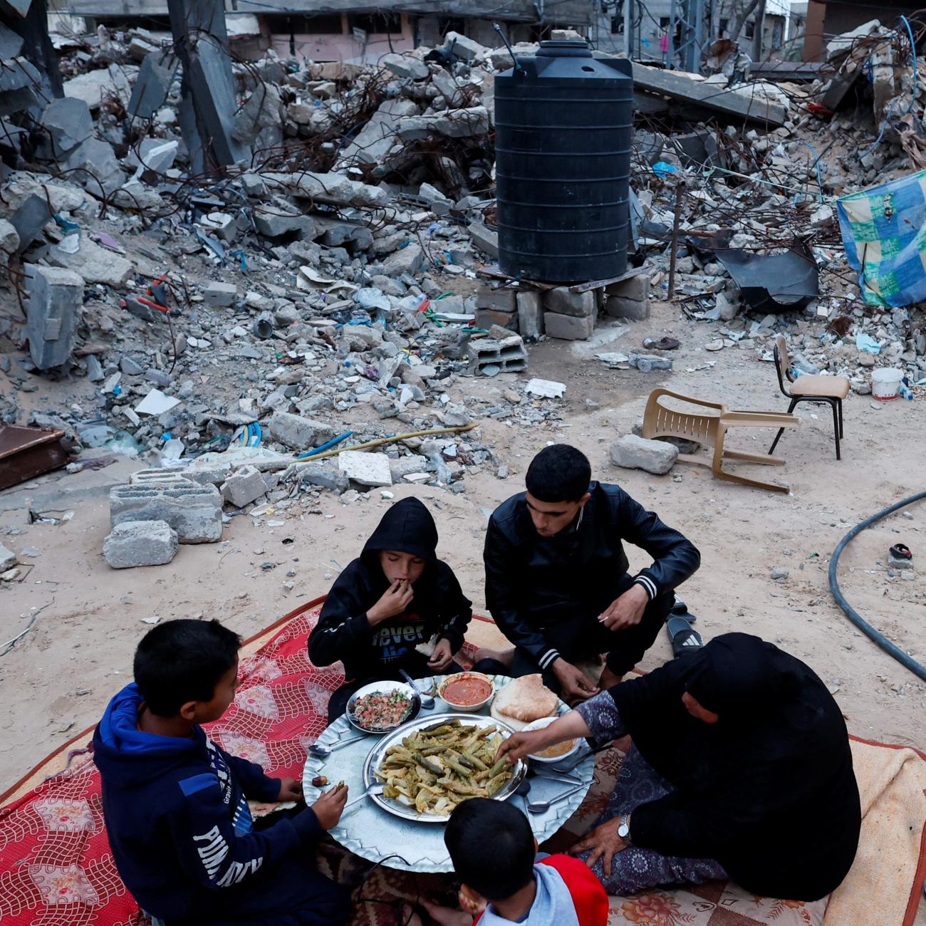 A Palestinian family eats their iftar meal they break their fast near the rubble of their destroyed house.