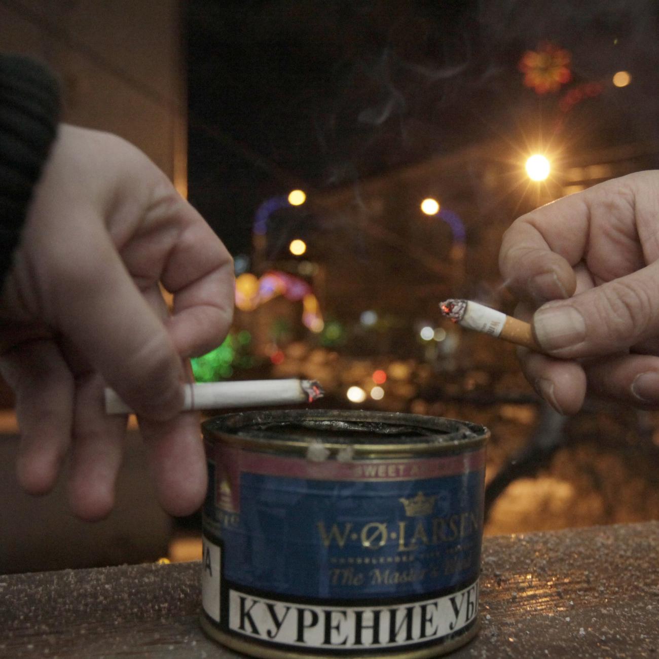 Men tap ash from their cigarettes while smoking on the balcony of an office building.