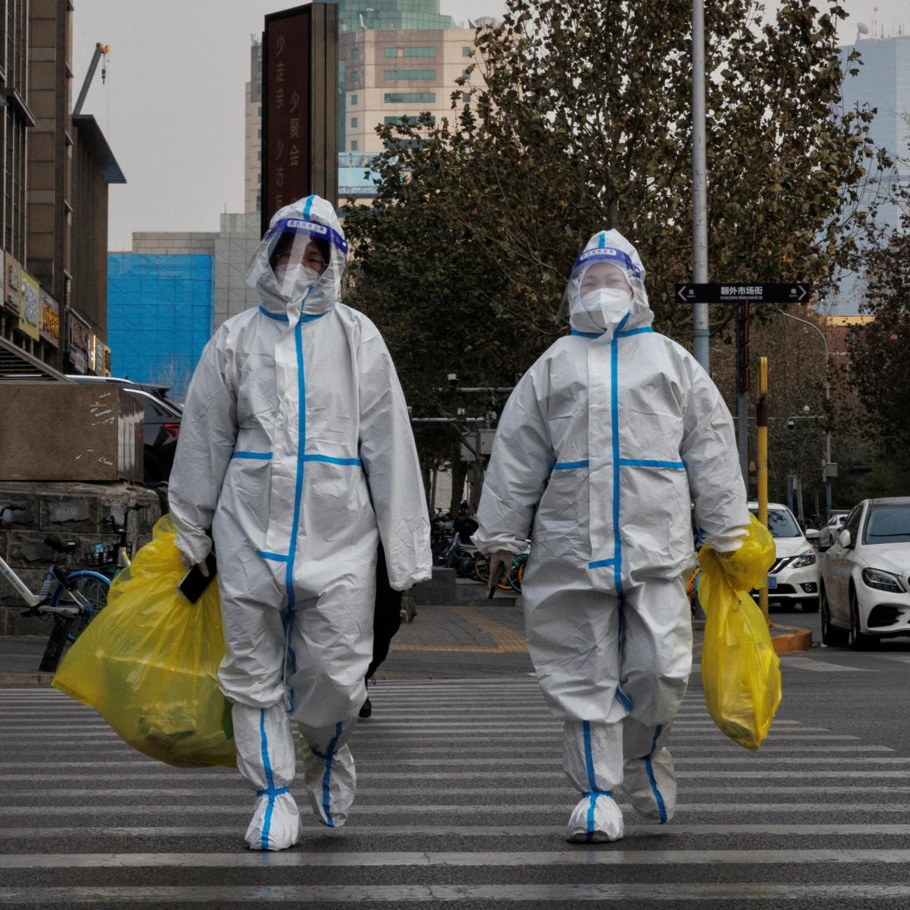 Pandemic prevention workers in protective suits cross a street as COVID-19 outbreaks continue.