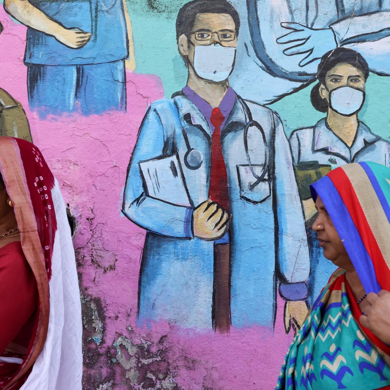 Women walk past a COVID-19 themed mural on the street.